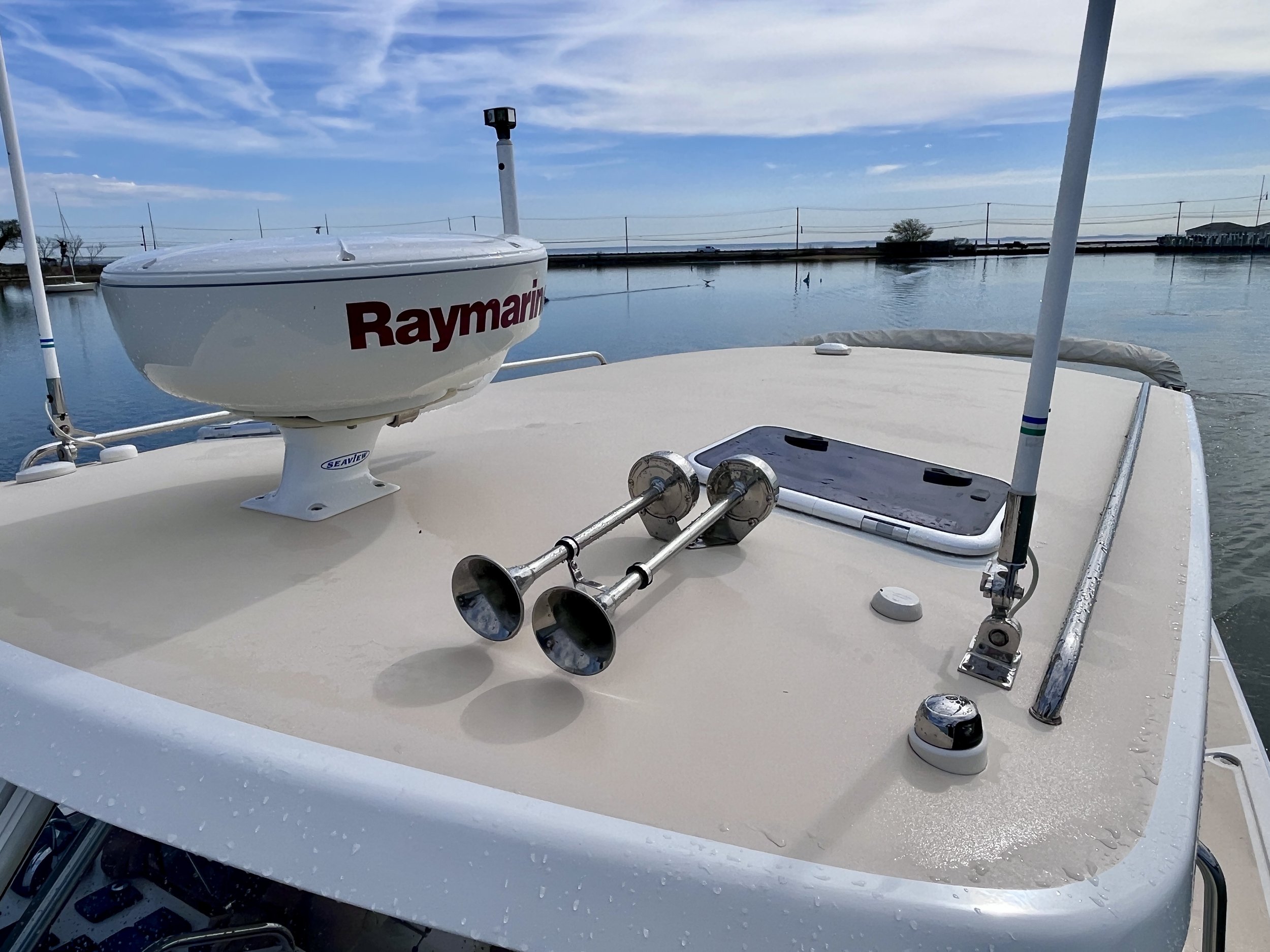 View from the boat showing a calm body of water with sailboats and a clear blue sky with wispy clouds, captured during the daytime.