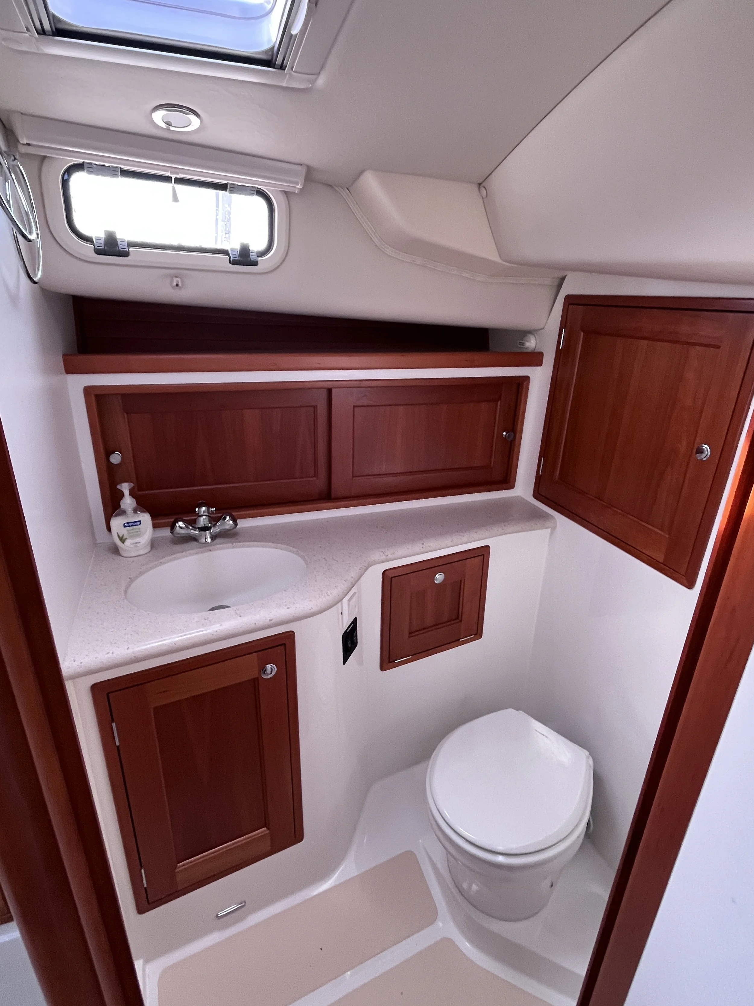 Small bathroom with a white toilet, wooden cabinets, a sink with a soap dispenser, and a window with a skylight above.