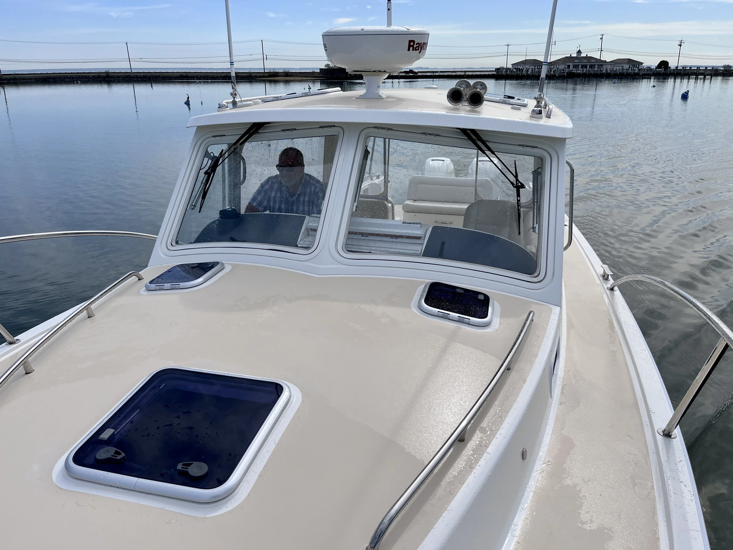 A boat on calm water with a cabin, a person inside wearing sunglasses, and a clear blue sky.