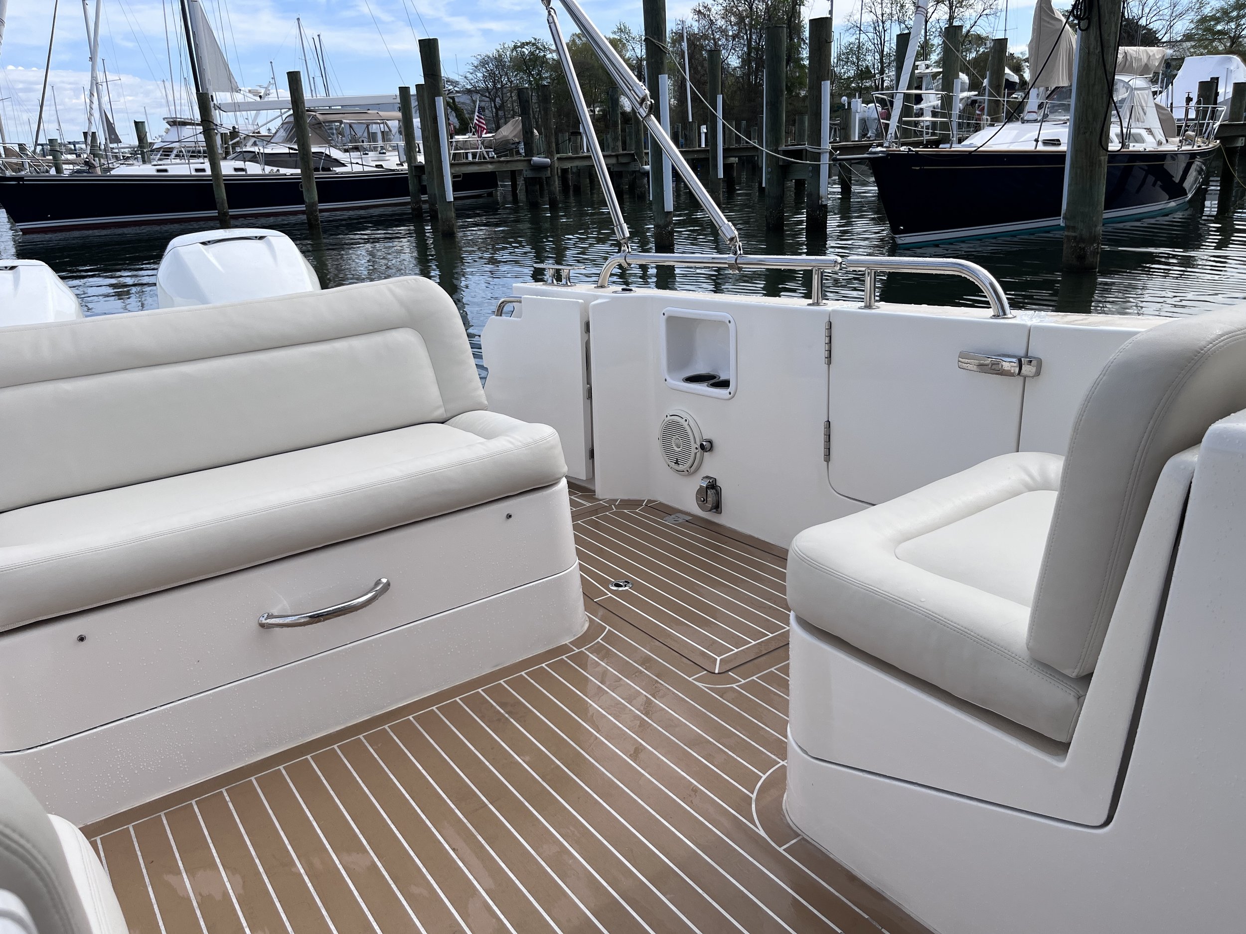 White cushioned seating area on a boat with a view of the marina and boats docked with sails, masts, and an American flag in the background.