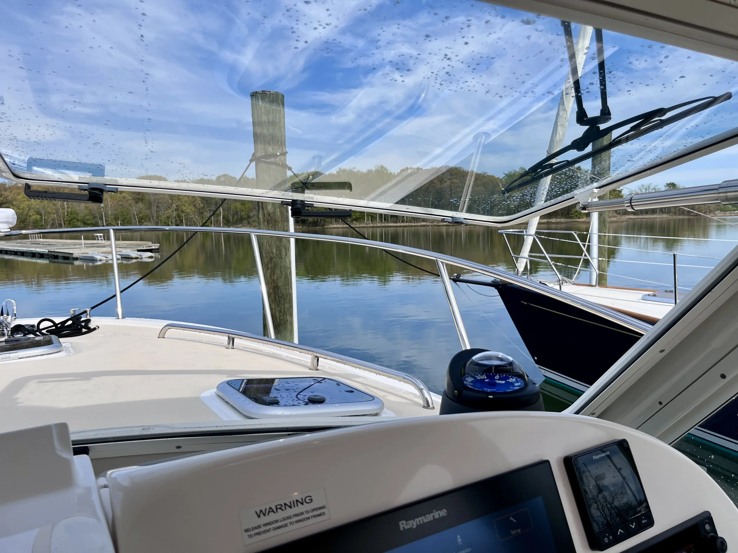 View from inside a boat looking out through a clear windshield covered in raindrops, with a lake and trees in the background.