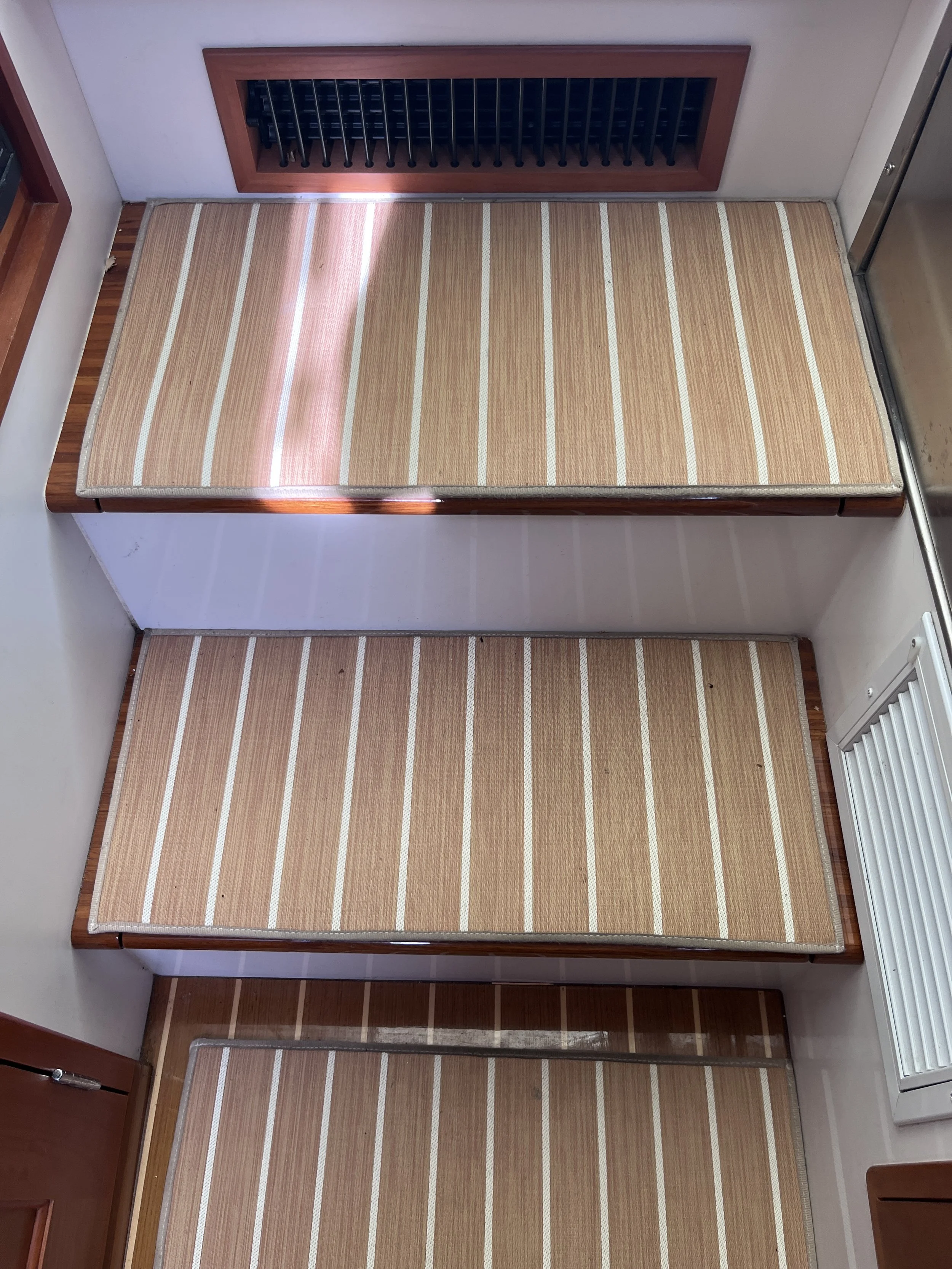 View of two wooden beds with striped beige and white mattresses, positioned in a small room with white walls and a carpeted floor.
