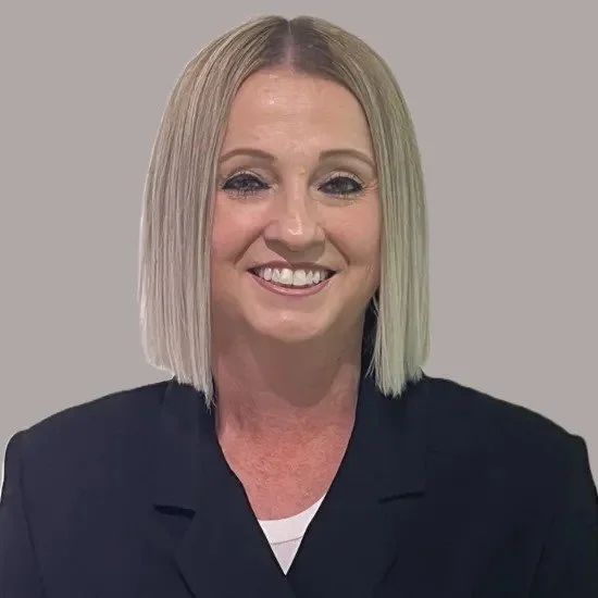 A smiling woman with shoulder-length blonde hair, wearing a dark blazer, against a gray background.