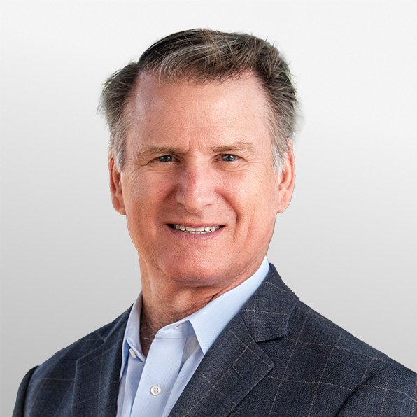 A middle-aged man with gray hair in business attire smiling at the camera against a plain light gray background.