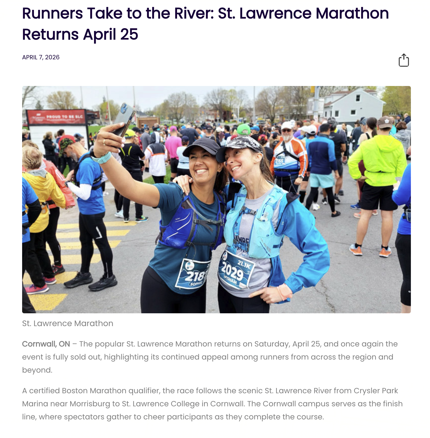 Two women taking a selfie at a crowded marathon event, with many runners and spectators in the background.