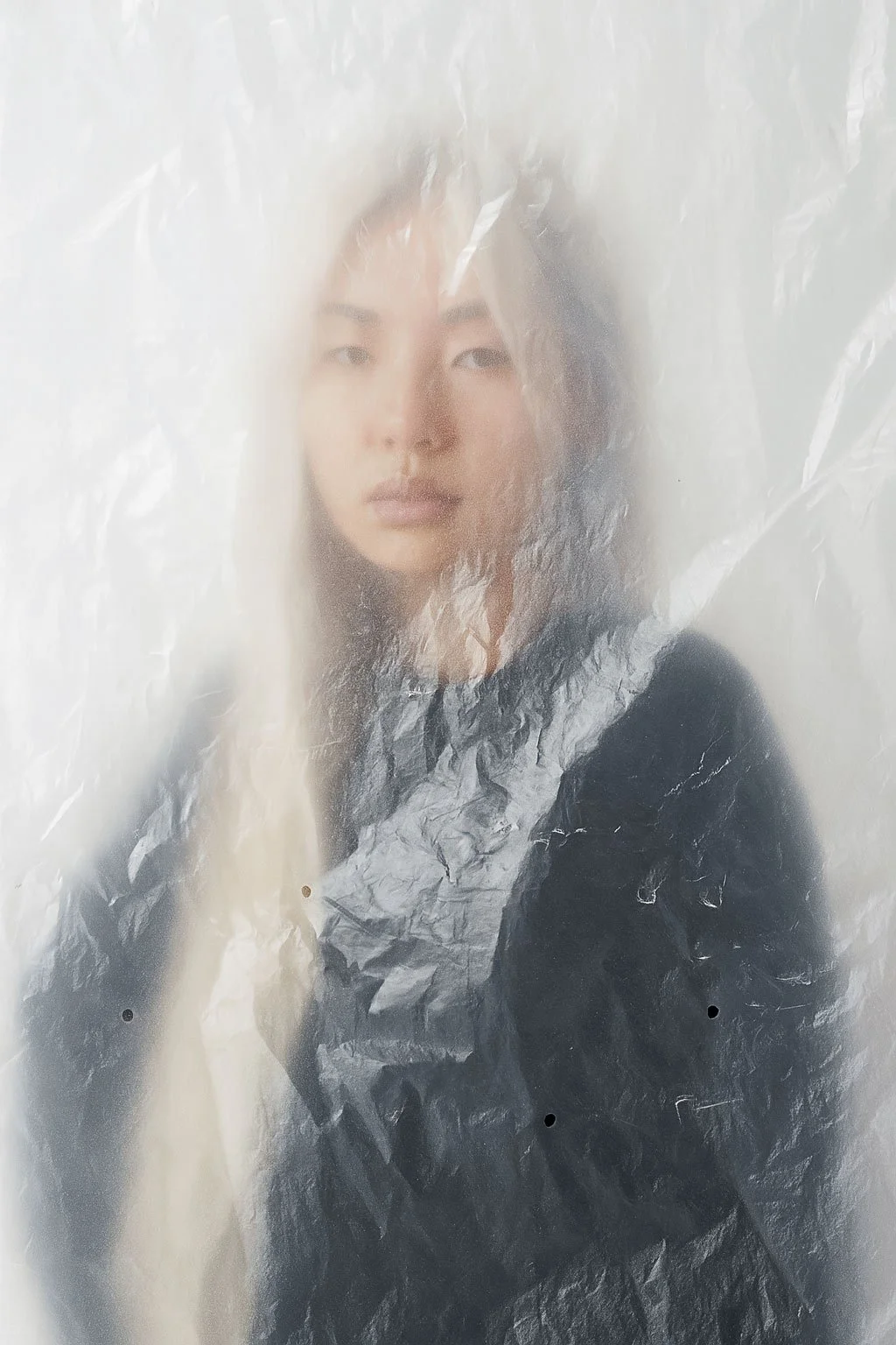 A woman's face seen through a semi-transparent, crinkled plastic sheet.