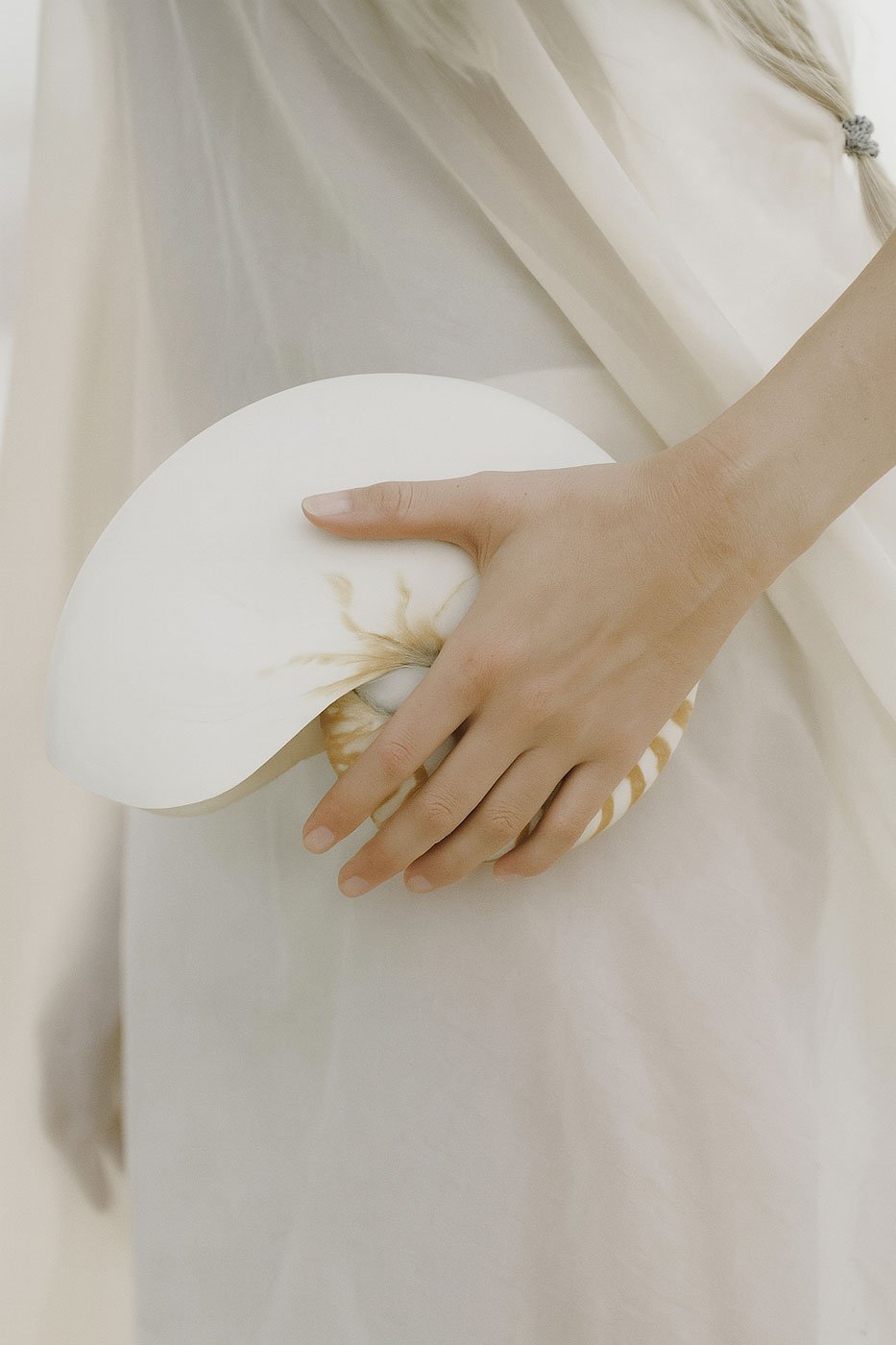 Person holding a shell with a white dish and fabric background.