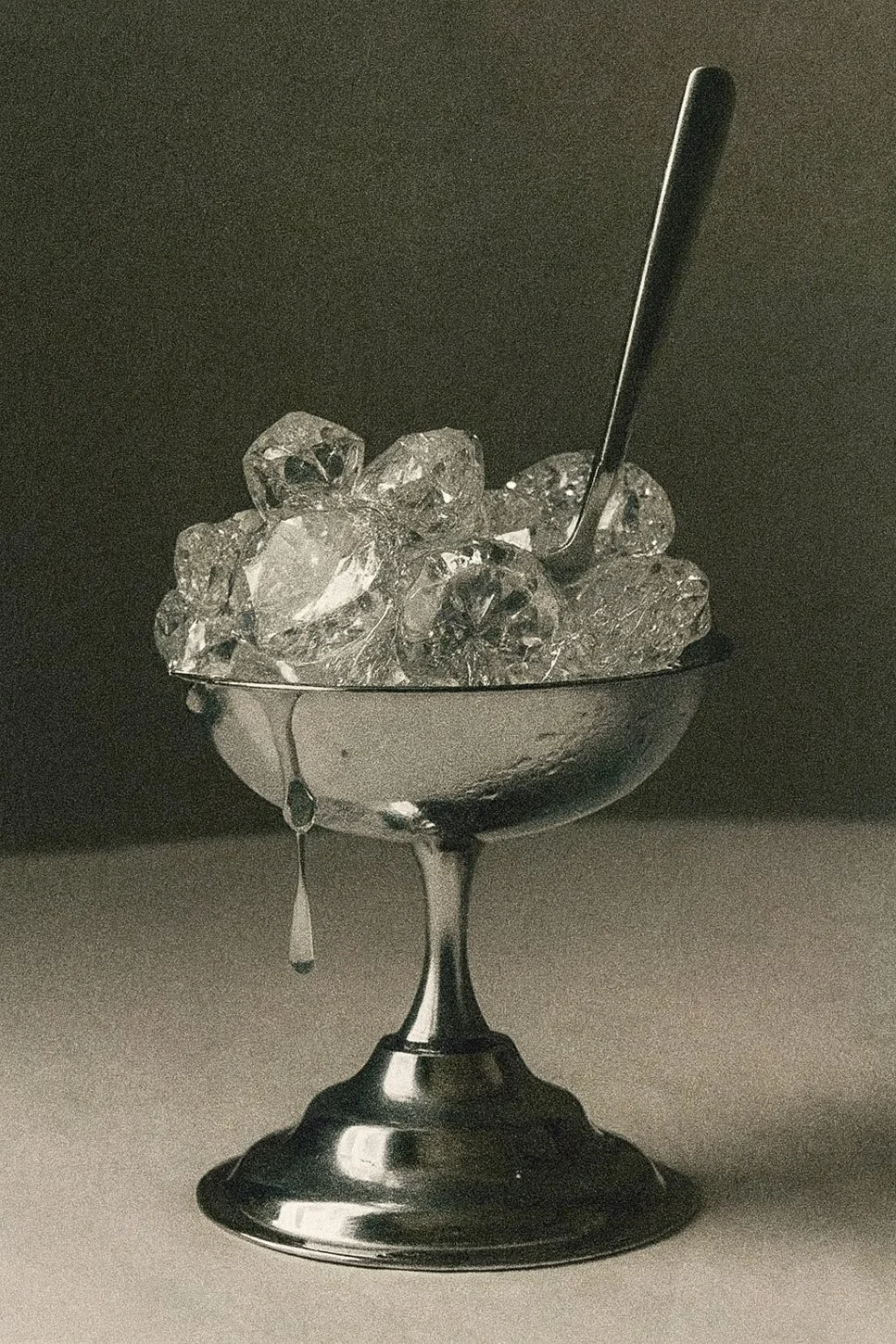 Silver cocktail glass filled with large ice cubes and a metal straw, with a droplet of melted ice hanging from the rim.