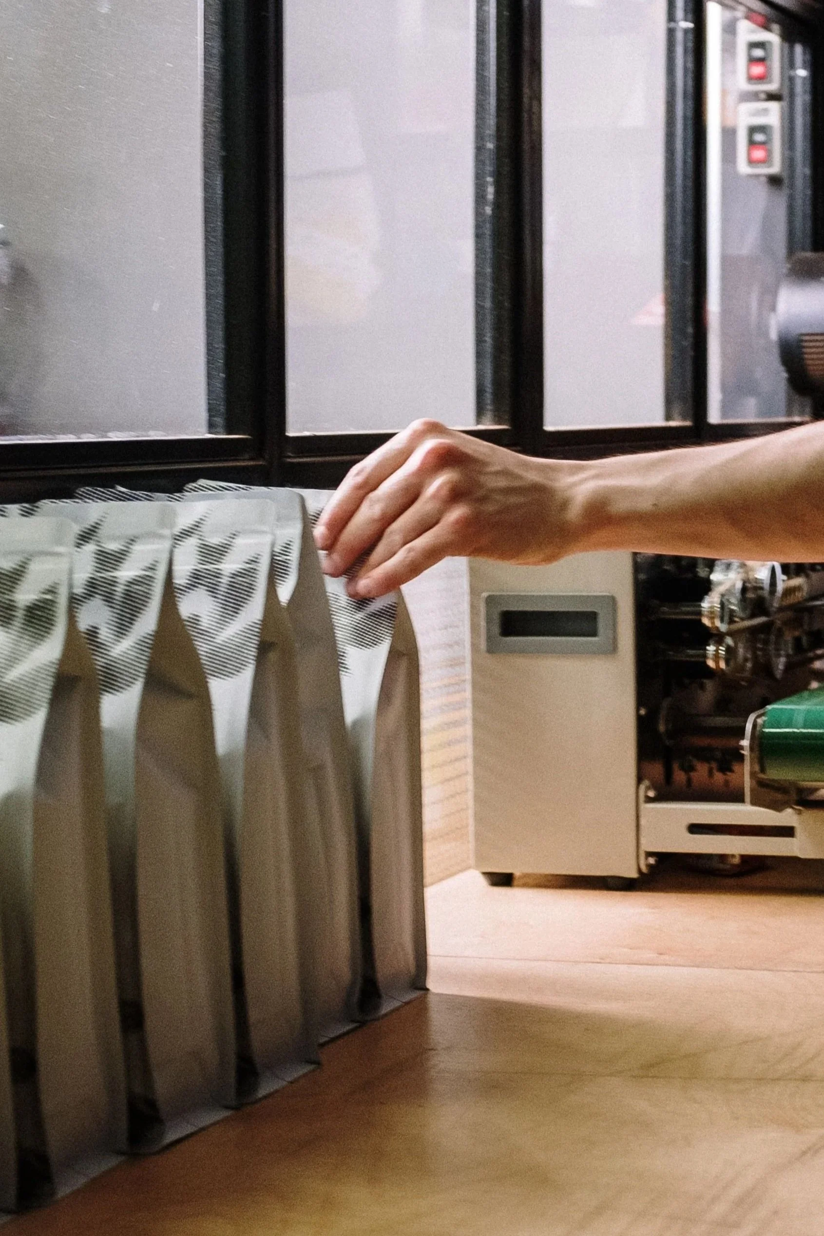 A hand reaching towards a row of books on a shelf in a library or bookstore, with a background of a counter and electronic devices.