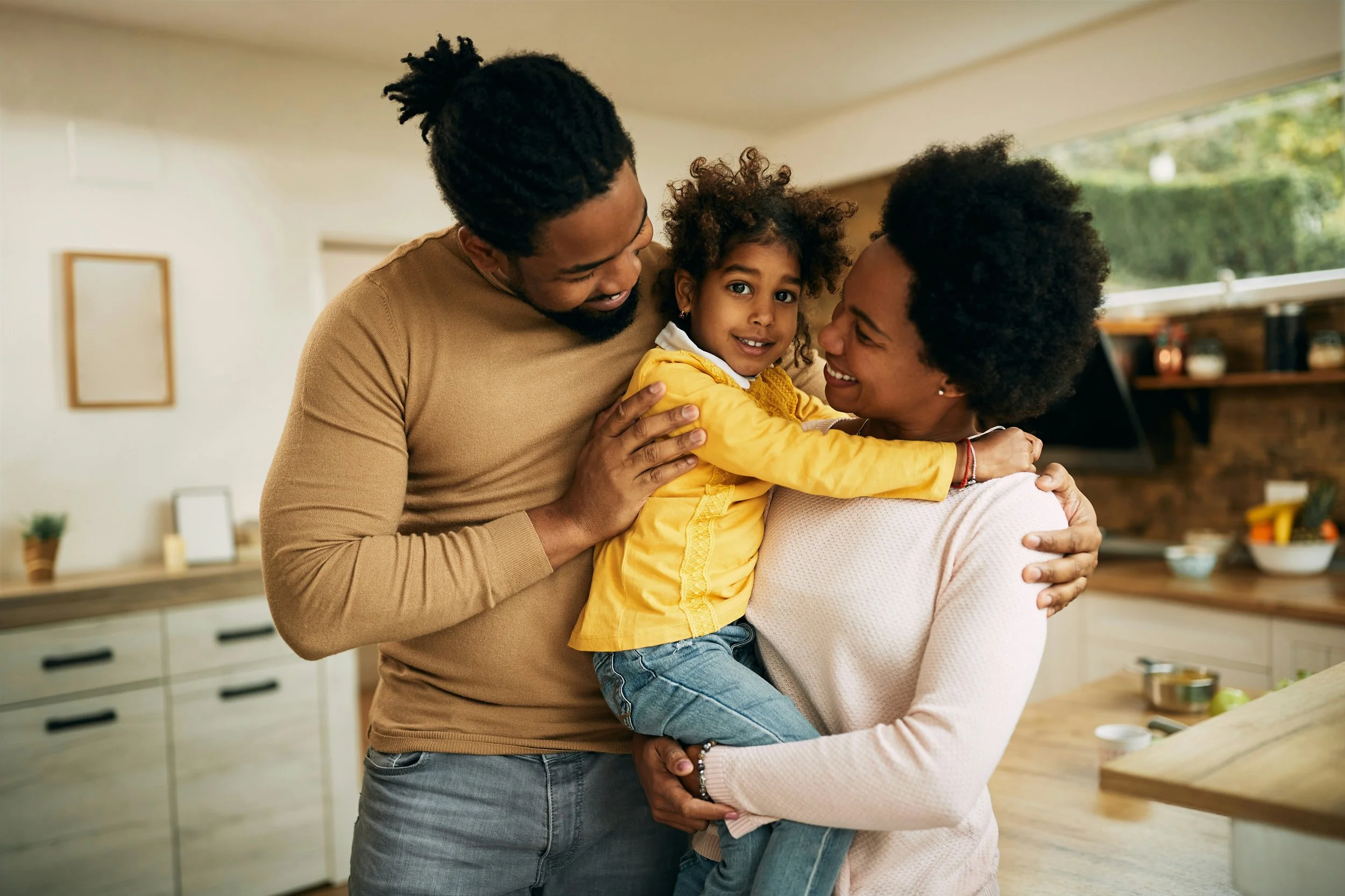 A happy multi-generational family in a modern kitchen, sharing a warm hug and smiling at each other.