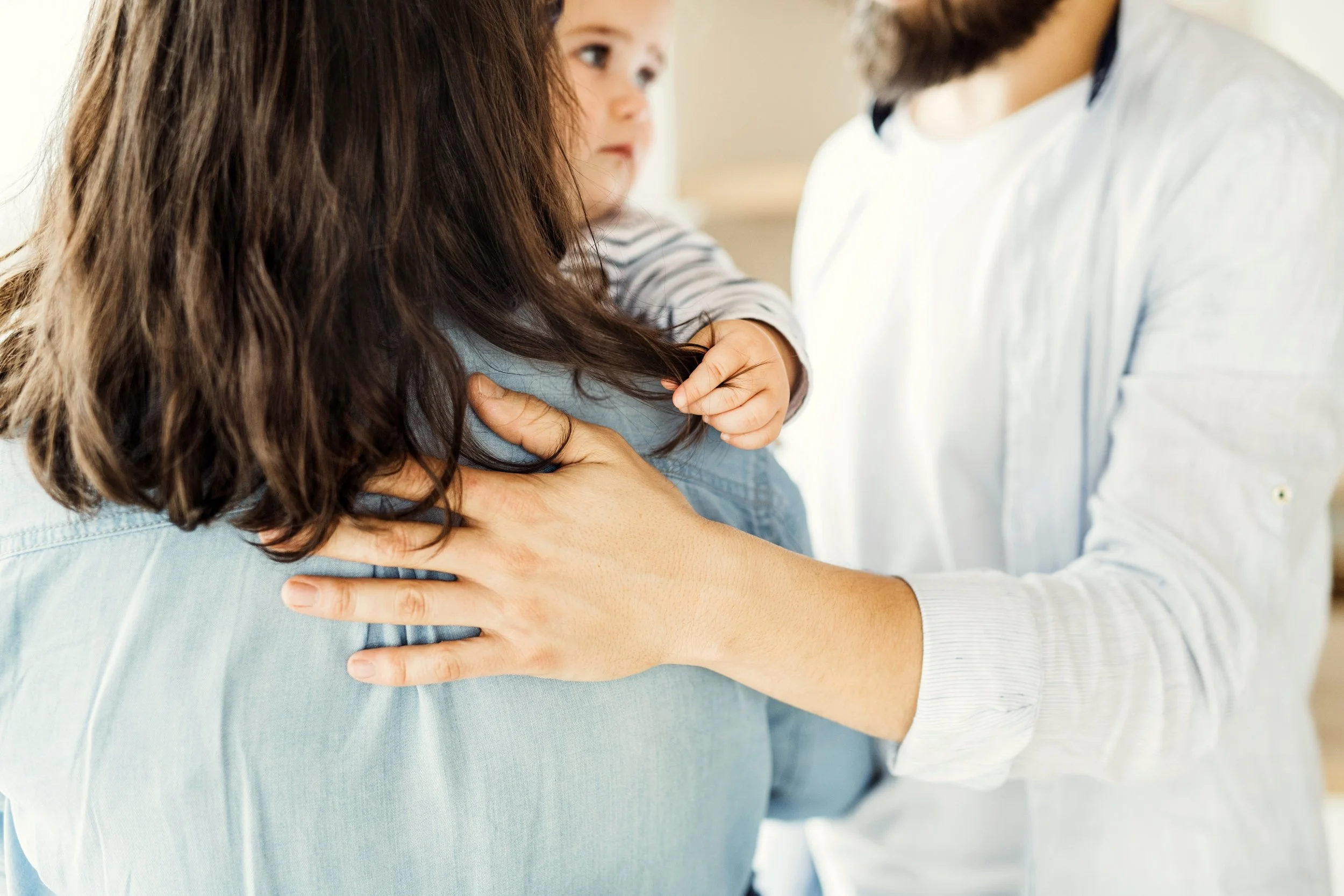 A close-up of a woman with long brown hair being embraced by a man, with another child's face visible behind them.