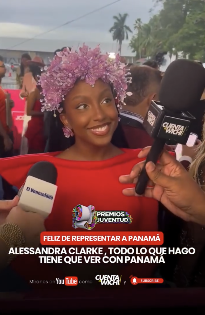 Young woman wearing a pink floral crown and red dress being interviewed by several reporters at an outdoor event.