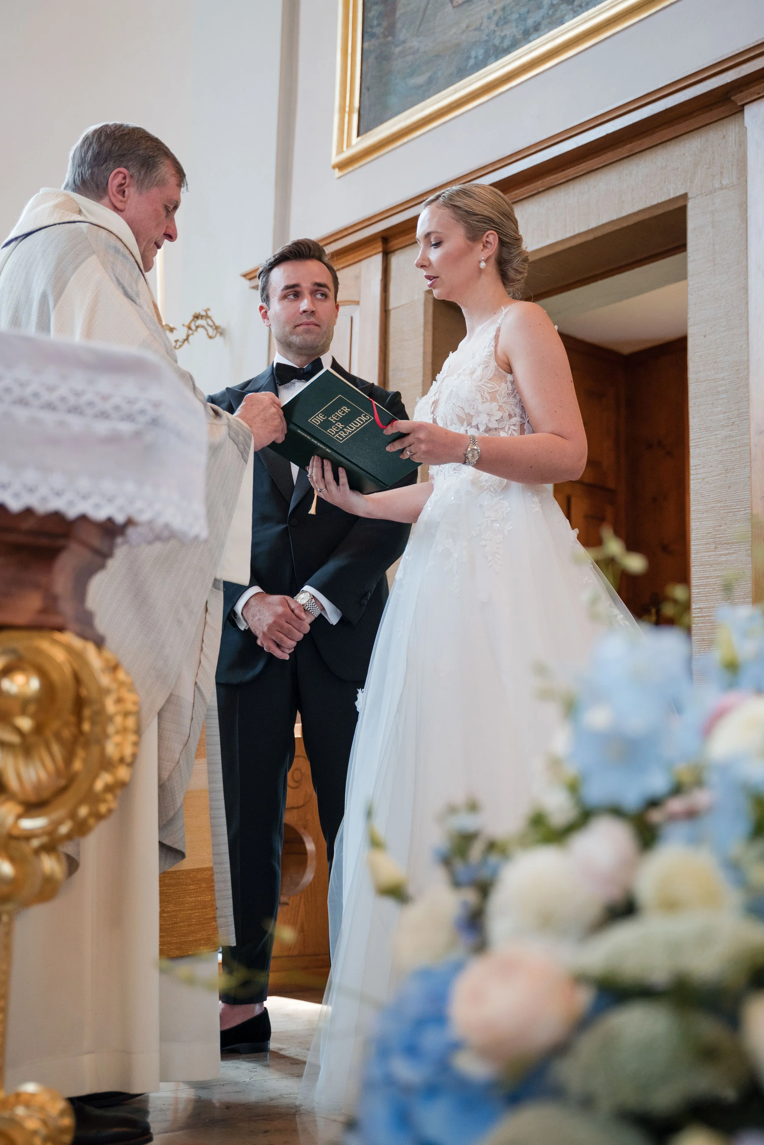 Ein Hochzeitspaar steht bei einer kirchlichen Trauung, der Bräutigam in Anzug und die Braut in einem weißen Kleid, bei einem Ringtausch.