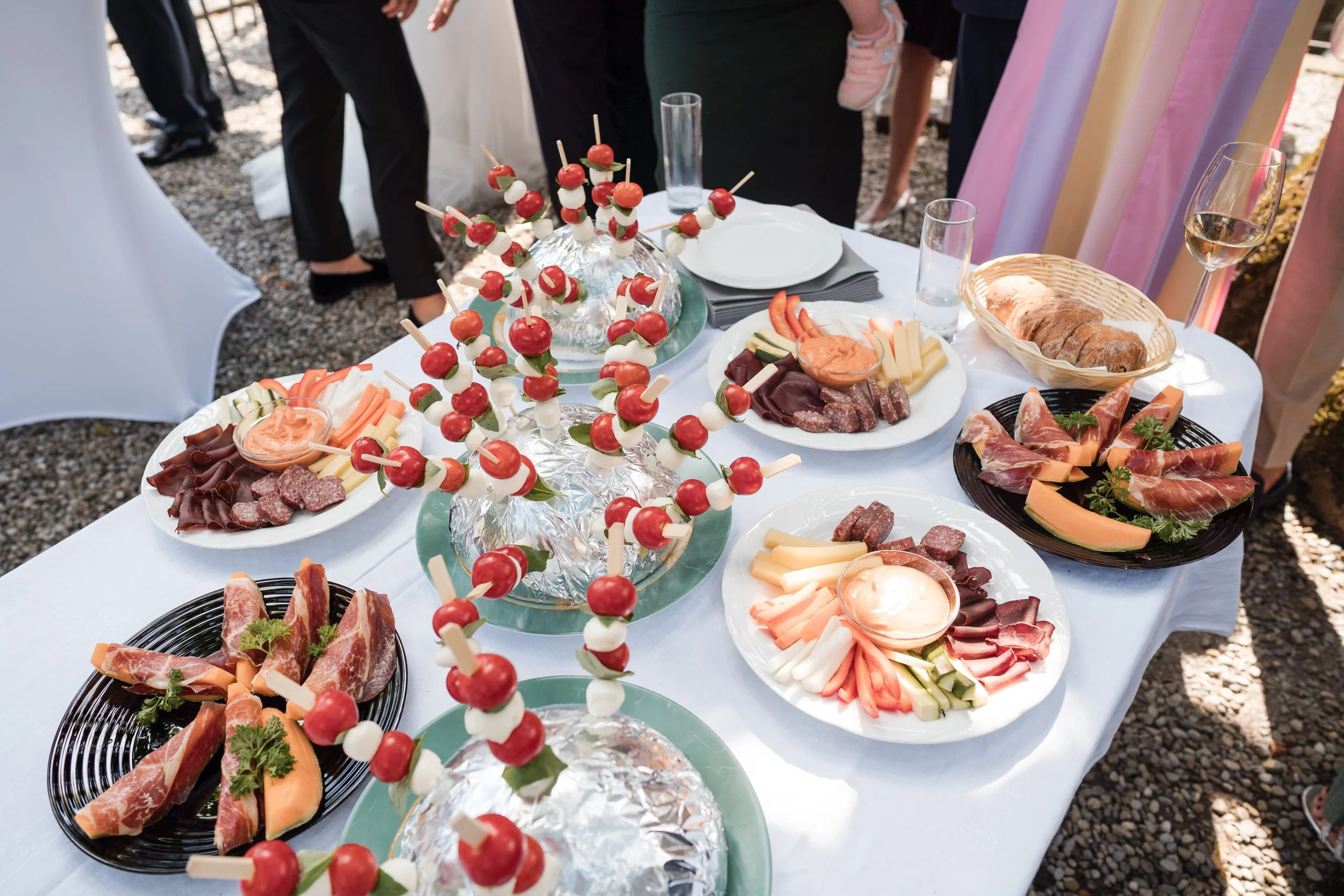 Ein Buffet mit verschiedenen Antipasti, Käse, Wurst, Oliven, Brot und Tomaten auf Spießen bei einem outdoor Event.