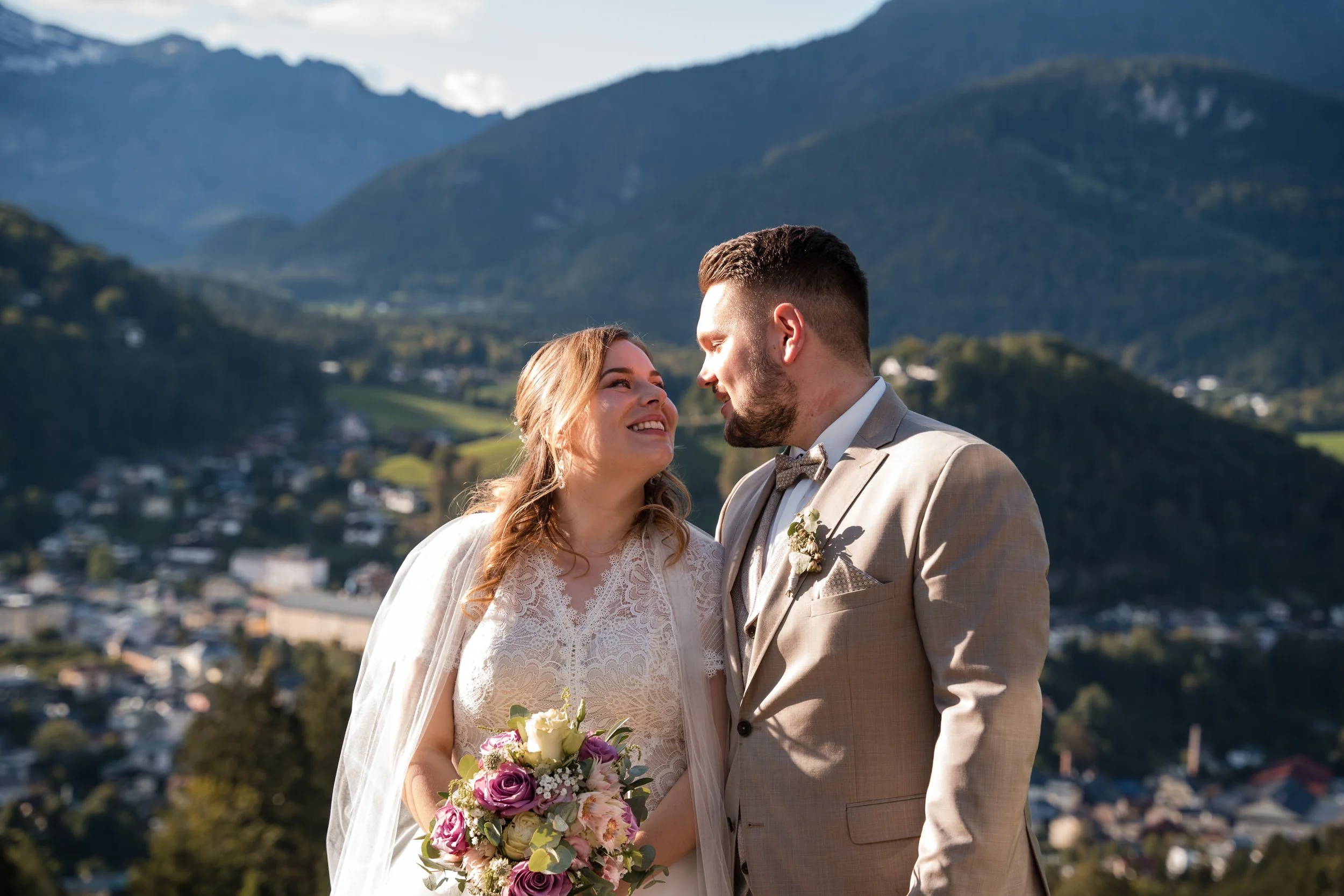 Braut und Bräutigam stehen sich bei ihrer Hochzeit im Freien gegenüber, mit Berglandschaft im Hintergrund.