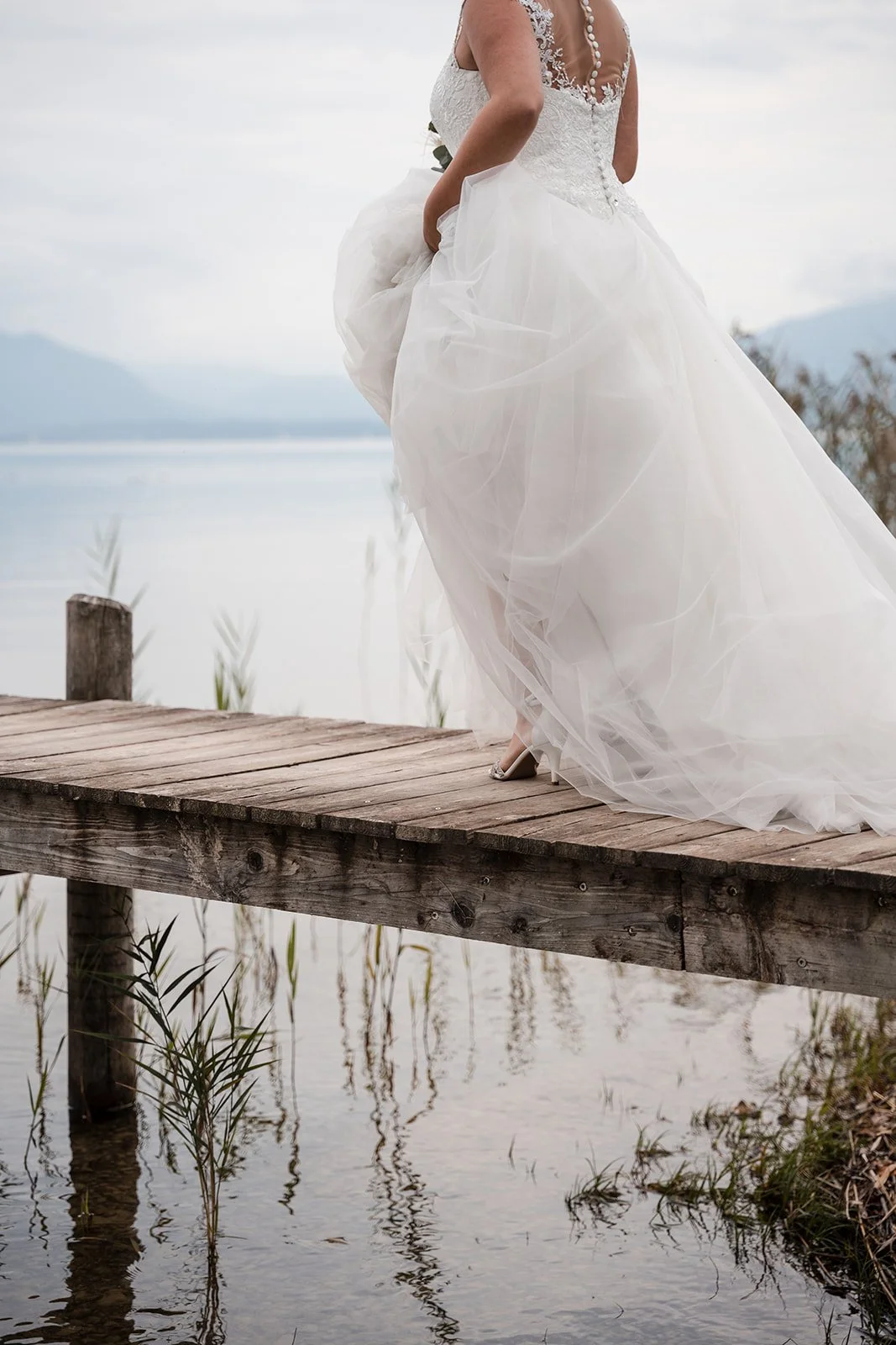 Braut in weißem Hochzeitskleid auf Holzsteg am Wasser