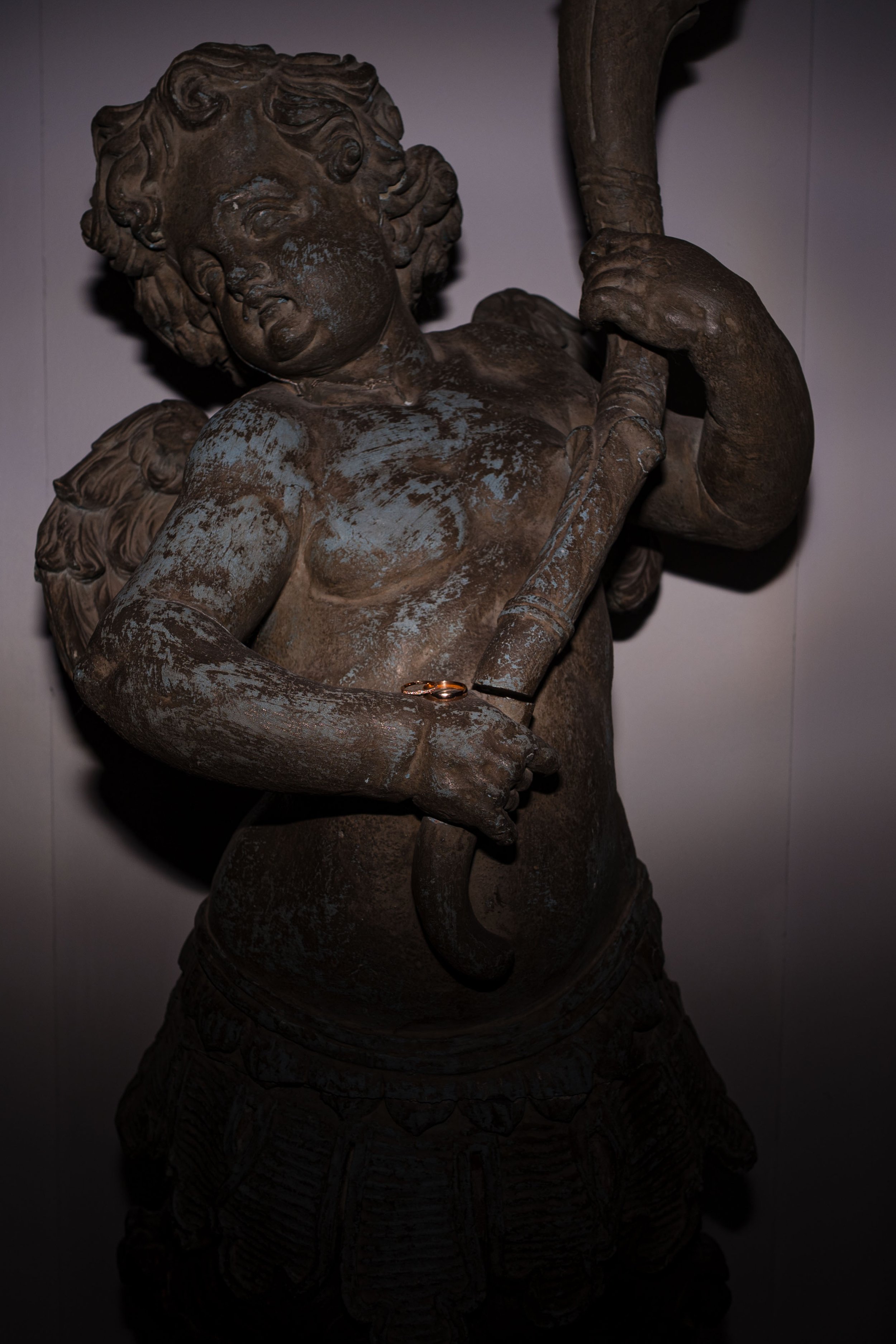 Eine alte Bronzestatue eines Jungen mit Flügeln, der eine Armbrust hält. Ein Ehering liegt an seinem Handgelenk.
