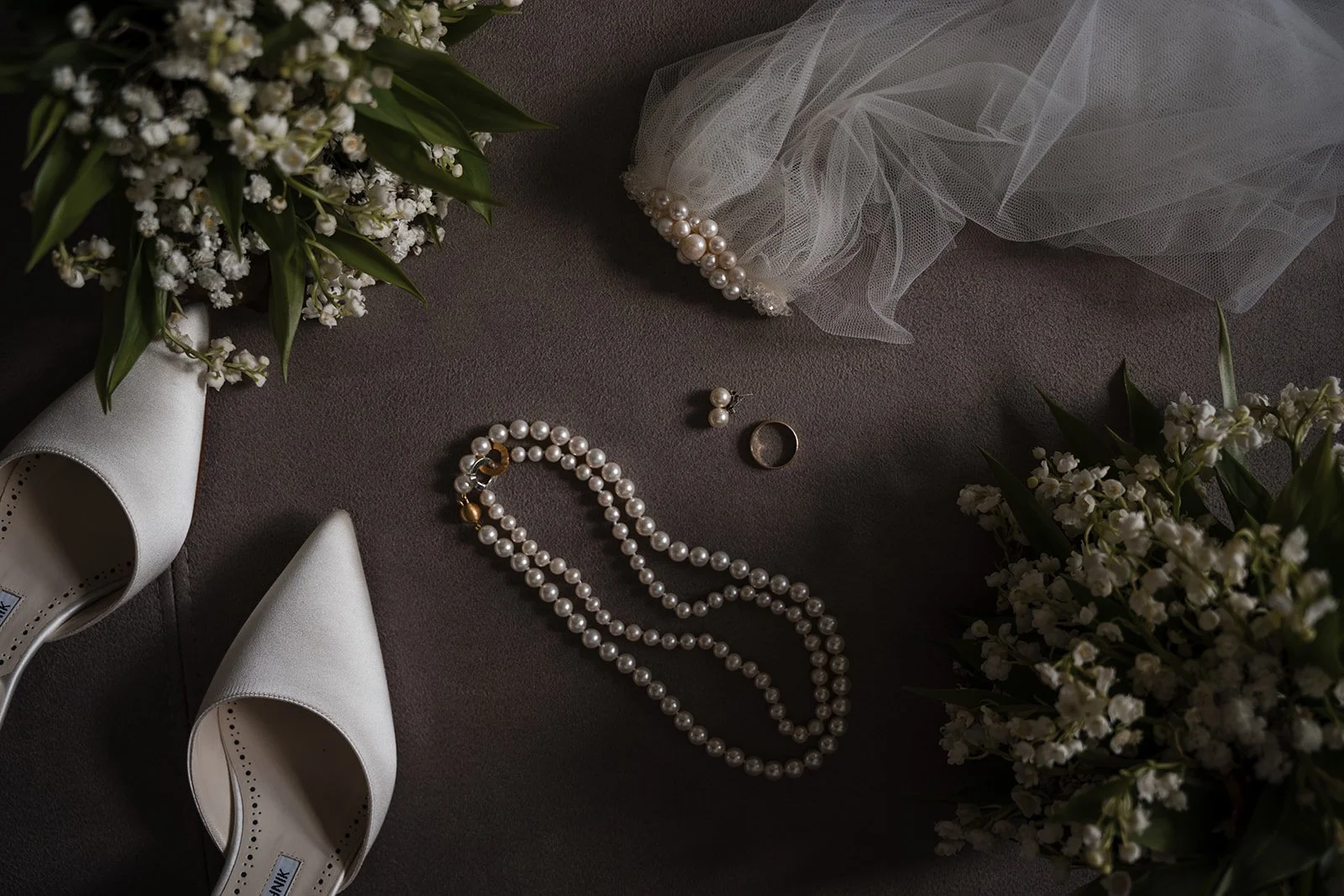 Brautschmuck, weiße Schuhe, Blumen und Tüllstoff auf dunklem Untergrund.