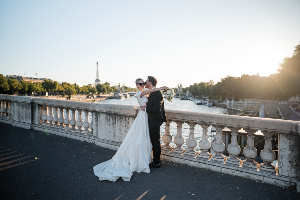 Braut und Bräutigam auf einer Brücke mit Blick auf die Seine und den Eiffelturm bei Sonnenuntergang in Paris.