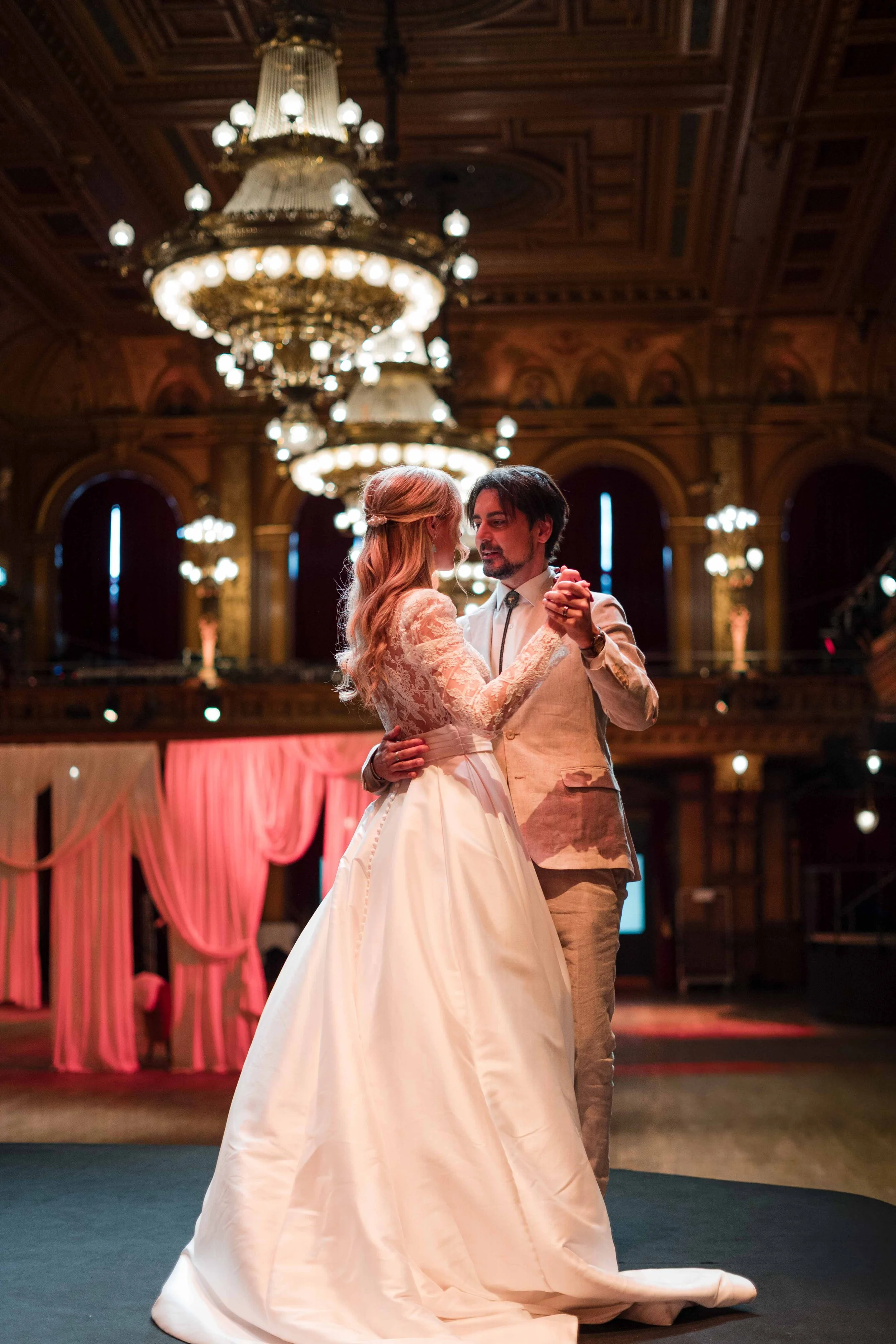 Ein Paar tanzt auf einer Hochzeit in einem eleganten, opulenten Saal mit großen Kronleuchtern.