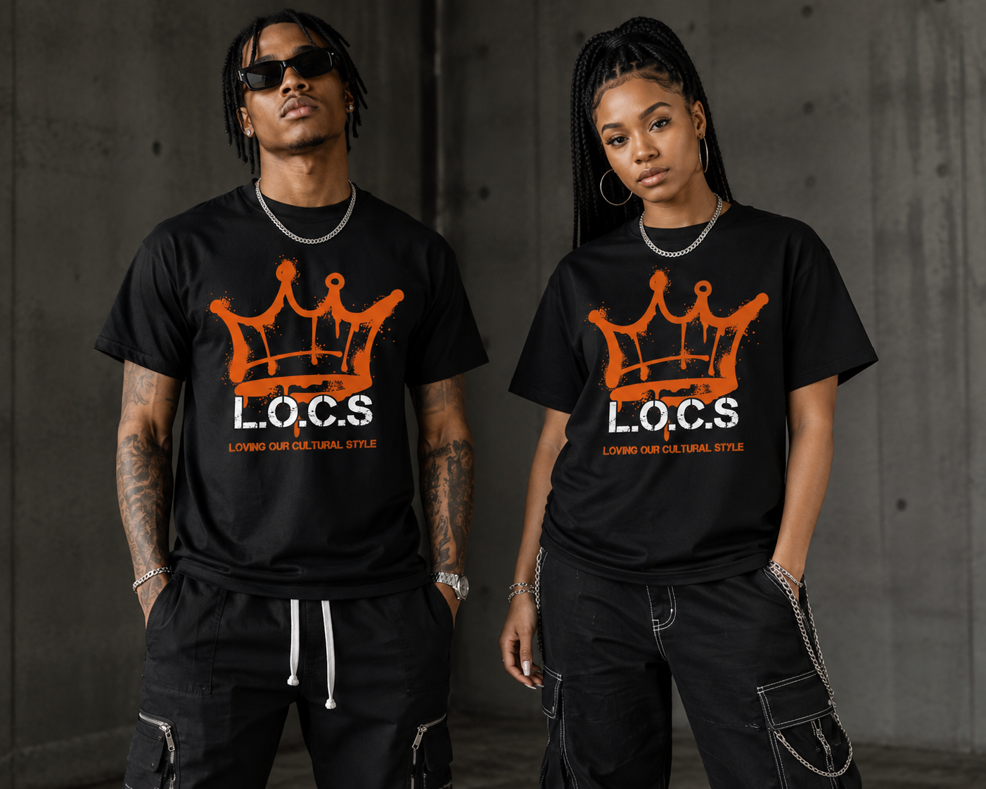A man and woman stand side by side wearing matching black T-shirts with graffiti-style orange crown and the text "L.O.C.S Loving Our Cultural Style". They are in an urban setting with a concrete wall background, both sporting jewelry and dark sunglasses.