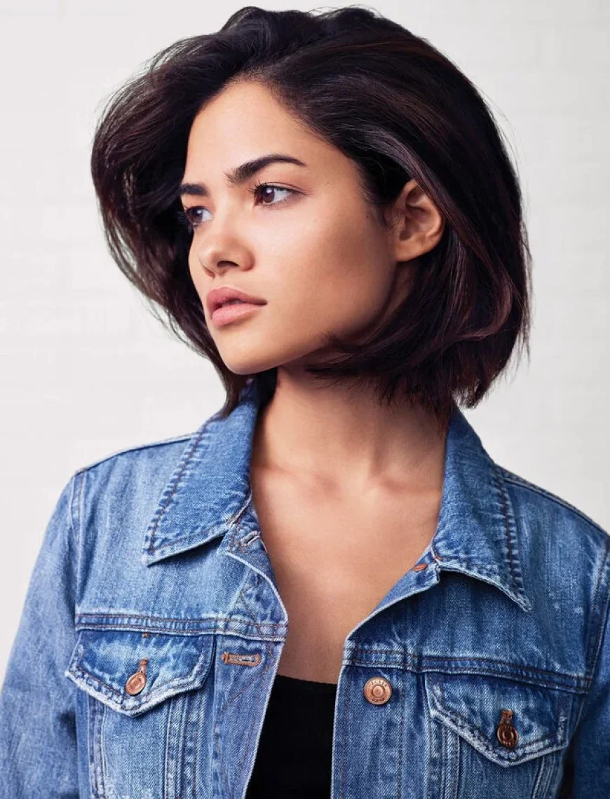 A woman with short dark hair wearing a denim jacket, looking to the side with a neutral expression.