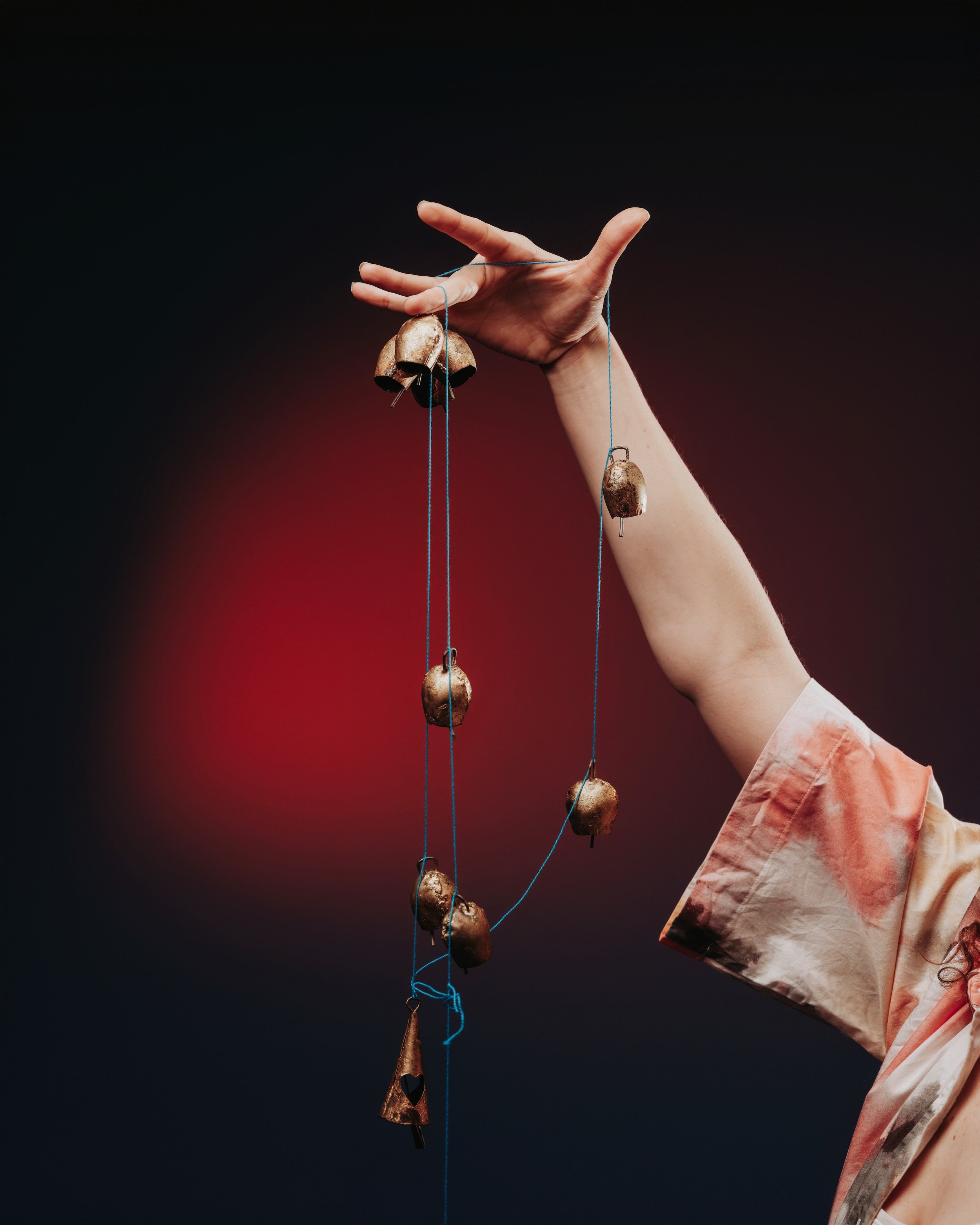 A close-up photo of an outstretched hand and arm holding several small bronze bells suspended from bright blue strings.