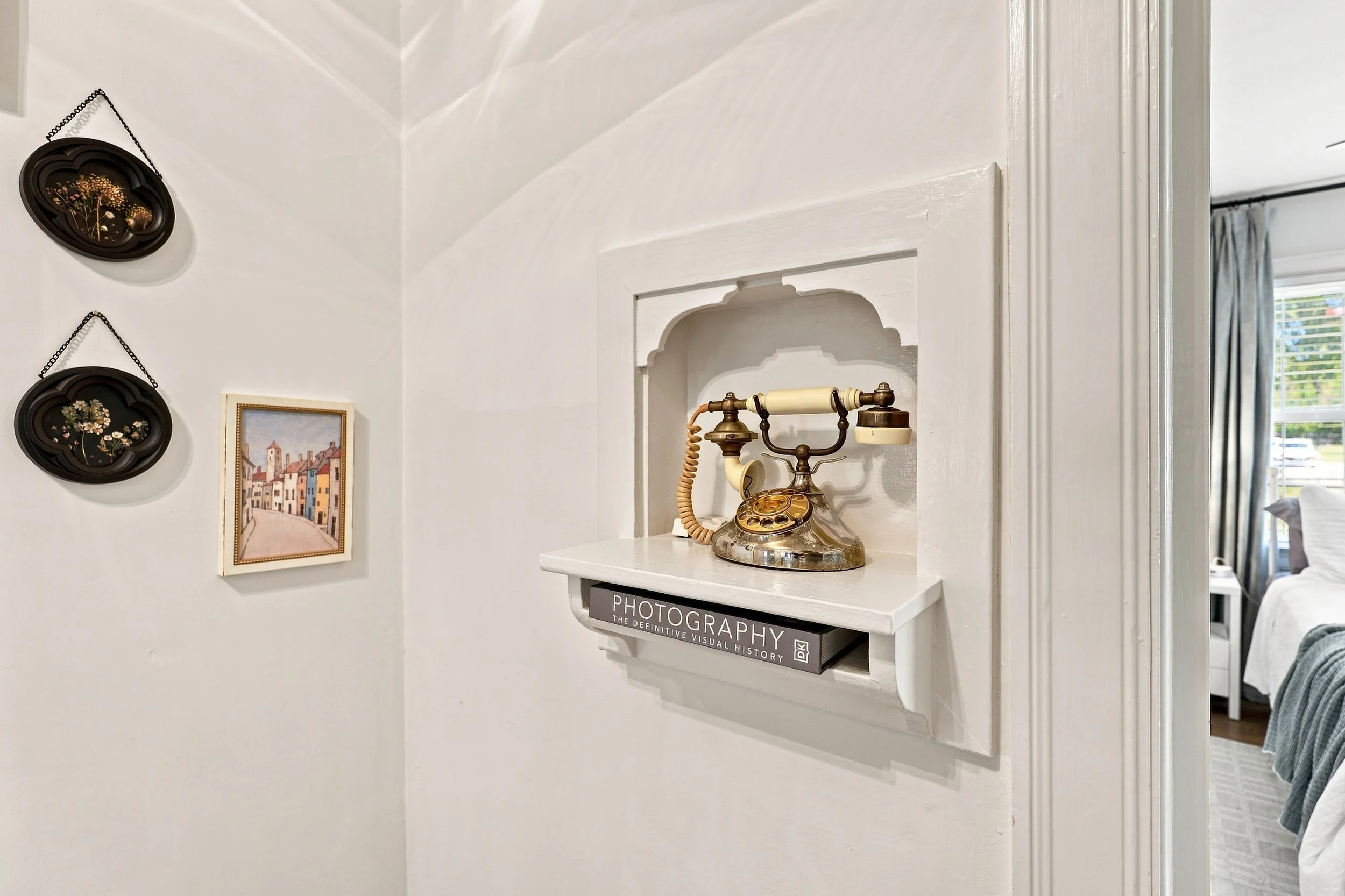 Vintage telephone on a white shelf in a room decorated with framed artwork and hanging decorative plates.
