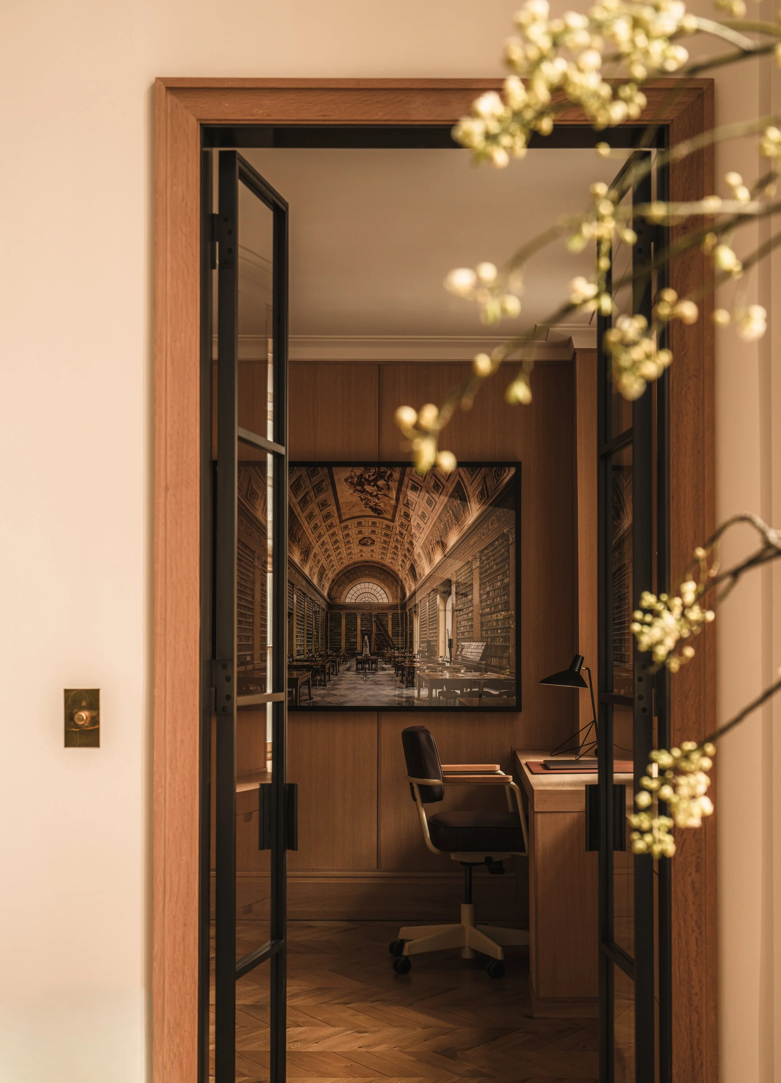 Refined home office featuring a wooden desk, black swivel chair, sculptural desk lamp and large-scale architectural artwork.