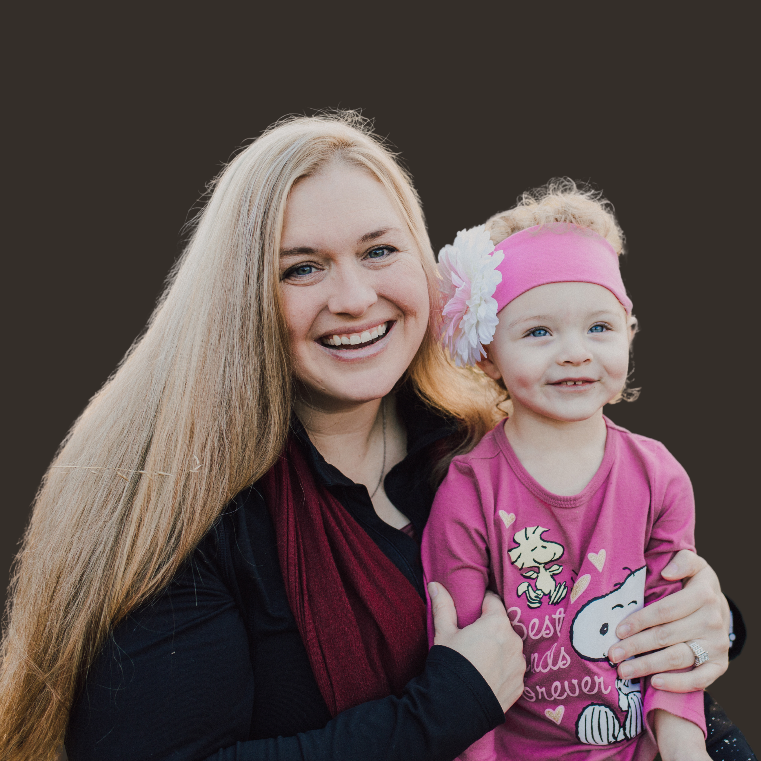 Close-up of a woman with long blonde hair and a young girl wearing a pink headband with flowers, both smiling and hugging, with a black background.