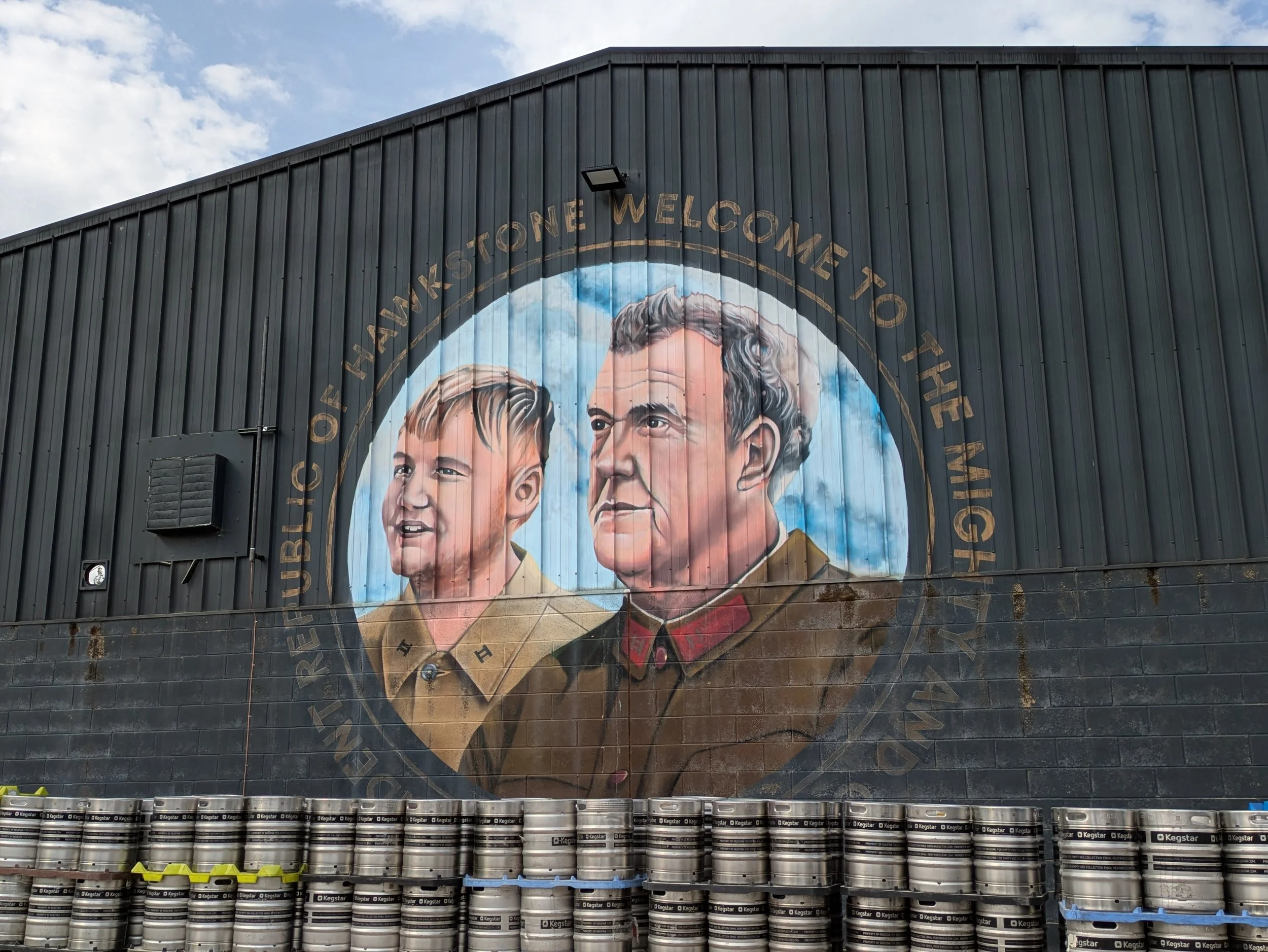 Wall mural of two men, one young and one older, with the text 'Bricklayers of Stone Welcome To' above their heads.