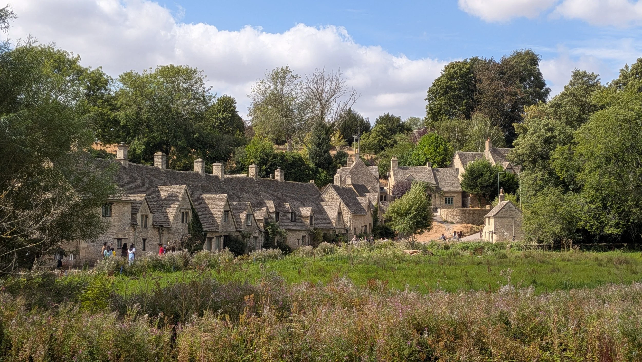 A scenic view of a village with stone houses and a lush green landscape under a partly cloudy sky.