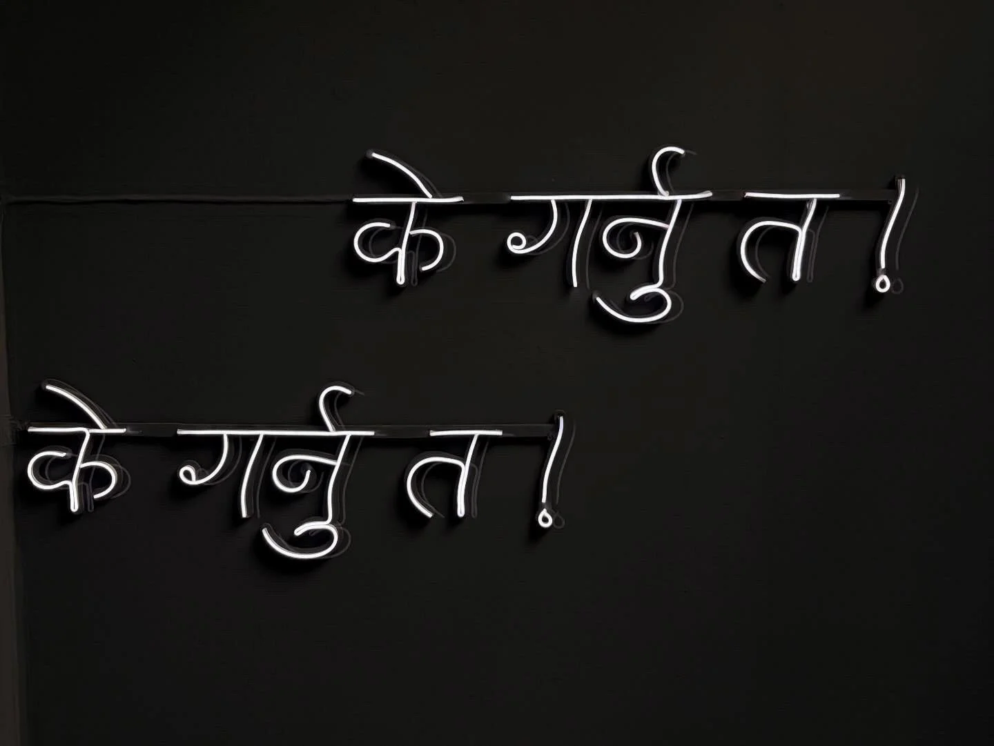 Neon sign in Hindi script that reads 'Kha Bunu!'. The sign is illuminated with white light against a black background.