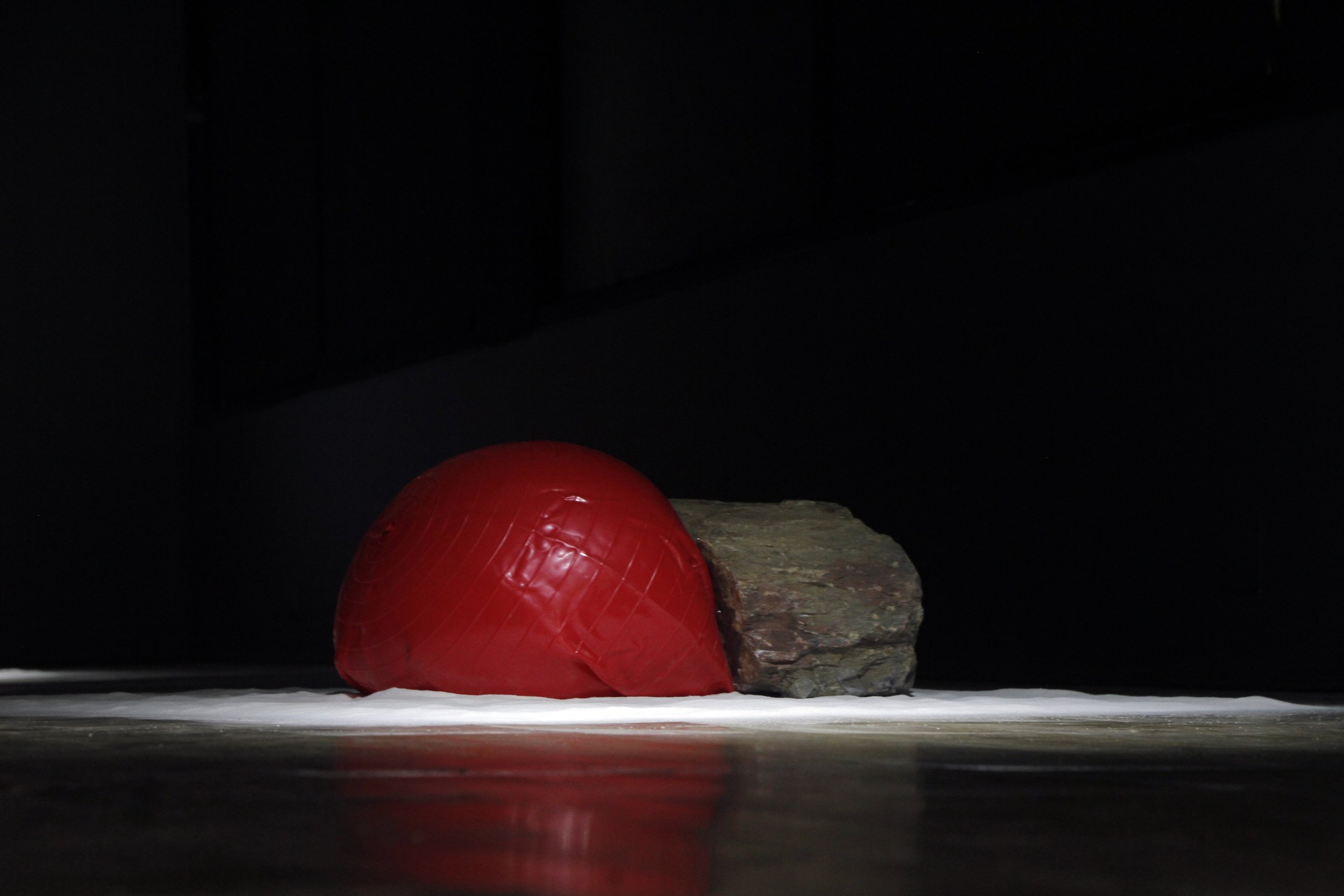 A red balloon sitting on a rocky surface with a dark background.