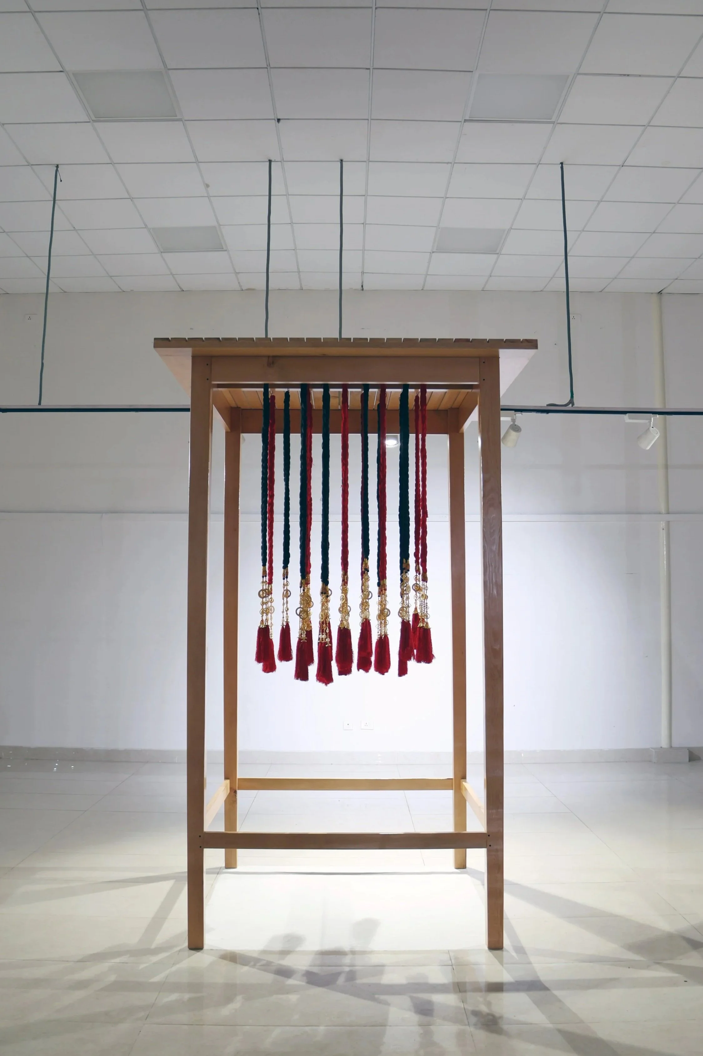 A wooden frame with hanging red and blue tassels inside a room with white walls and tiled ceiling.