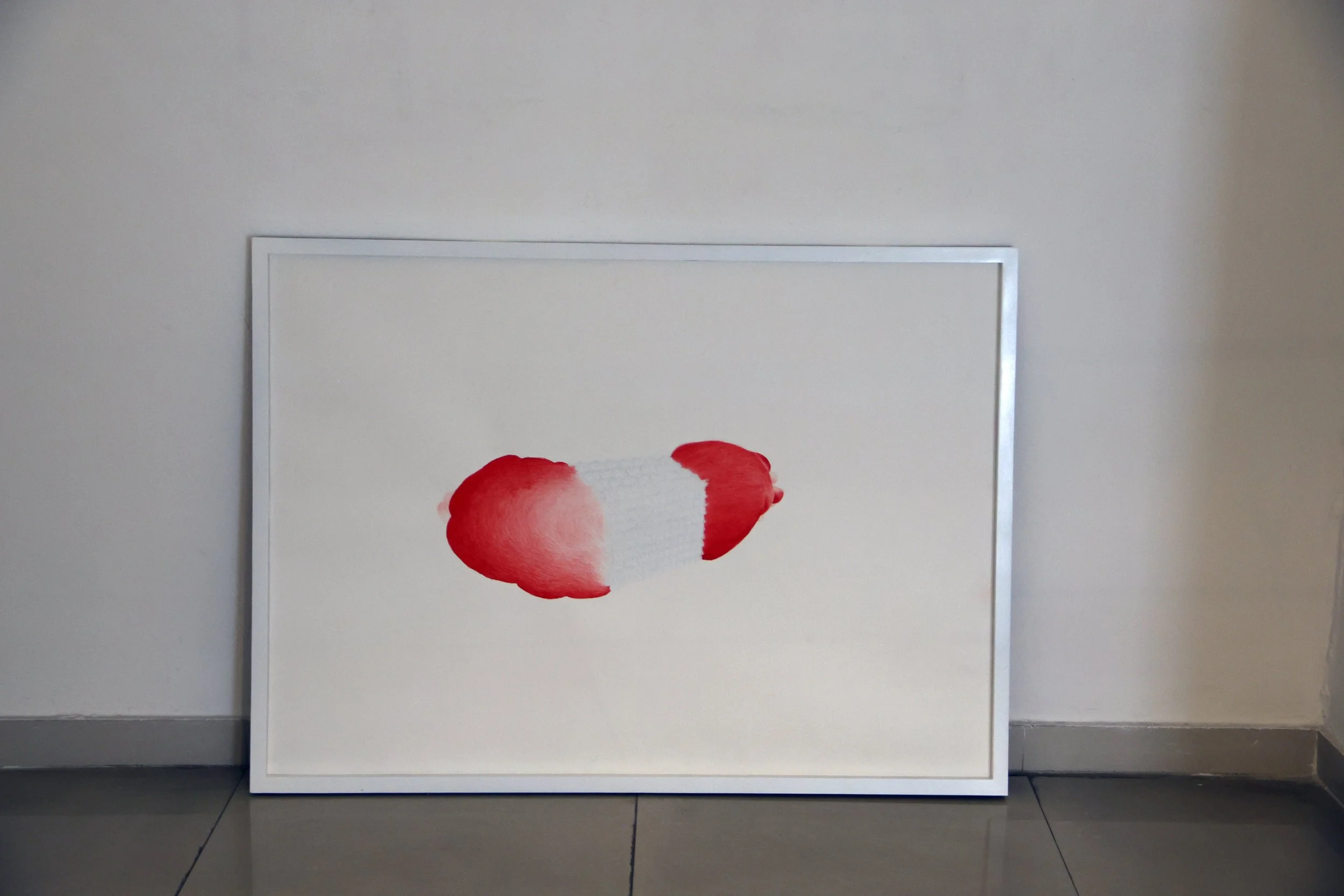 White framed artwork featuring a red watercolor stroke, leaning against a plain light-colored wall.