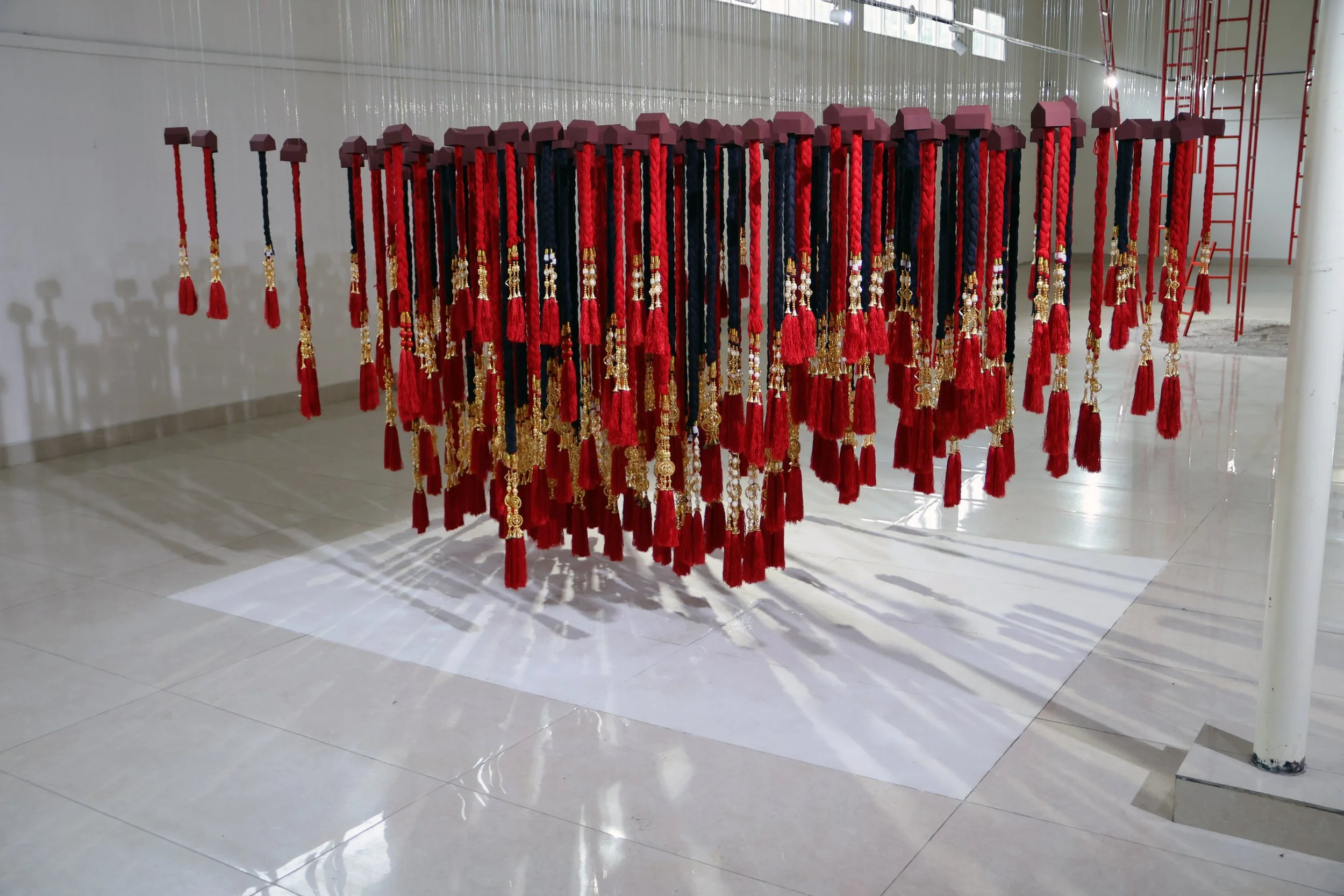 A display of multiple hanging cords with red, black, and dark blue colors, decorated with gold and pearl embellishments, supported by a metal frame in an indoor space with tiled floors and white walls.