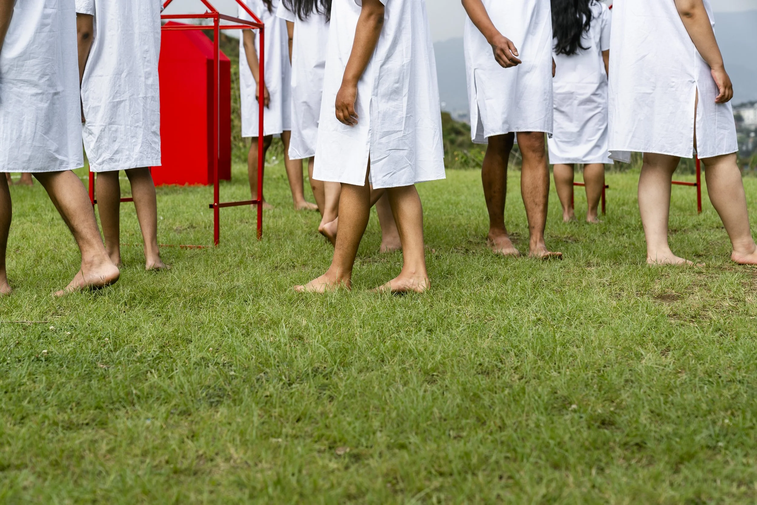 People in white gowns standing outdoors on grass, participating in an activity involving a red structure.