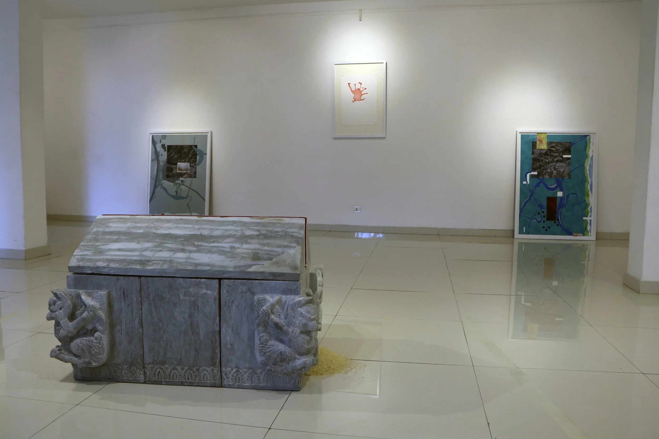 Art gallery with framed paintings on white walls and a carved stone bench in the foreground.