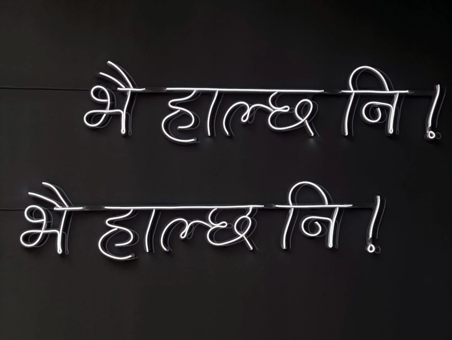 Neon sign in Devanagari script, illuminated in white, on a black background.