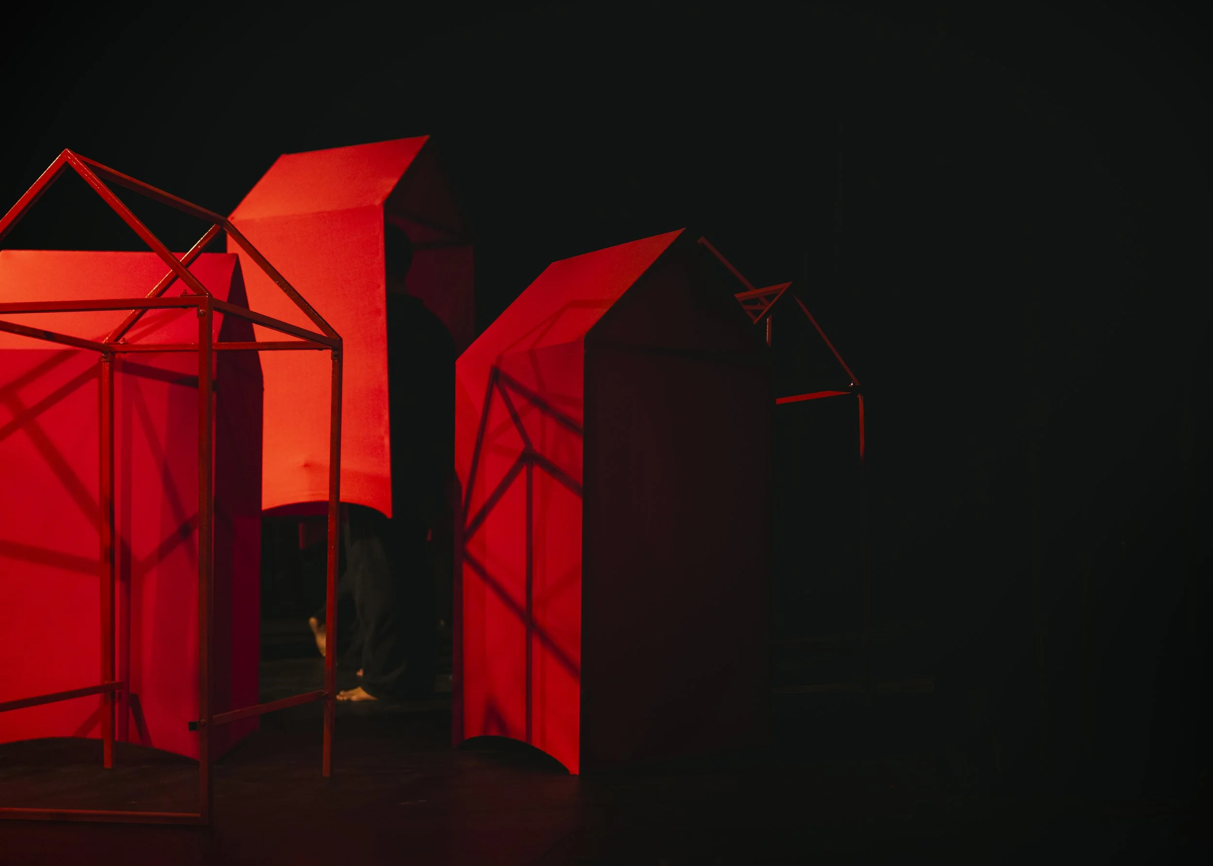 Abstract art installation consisting of red geometric shapes and structures illuminated in a dark setting.