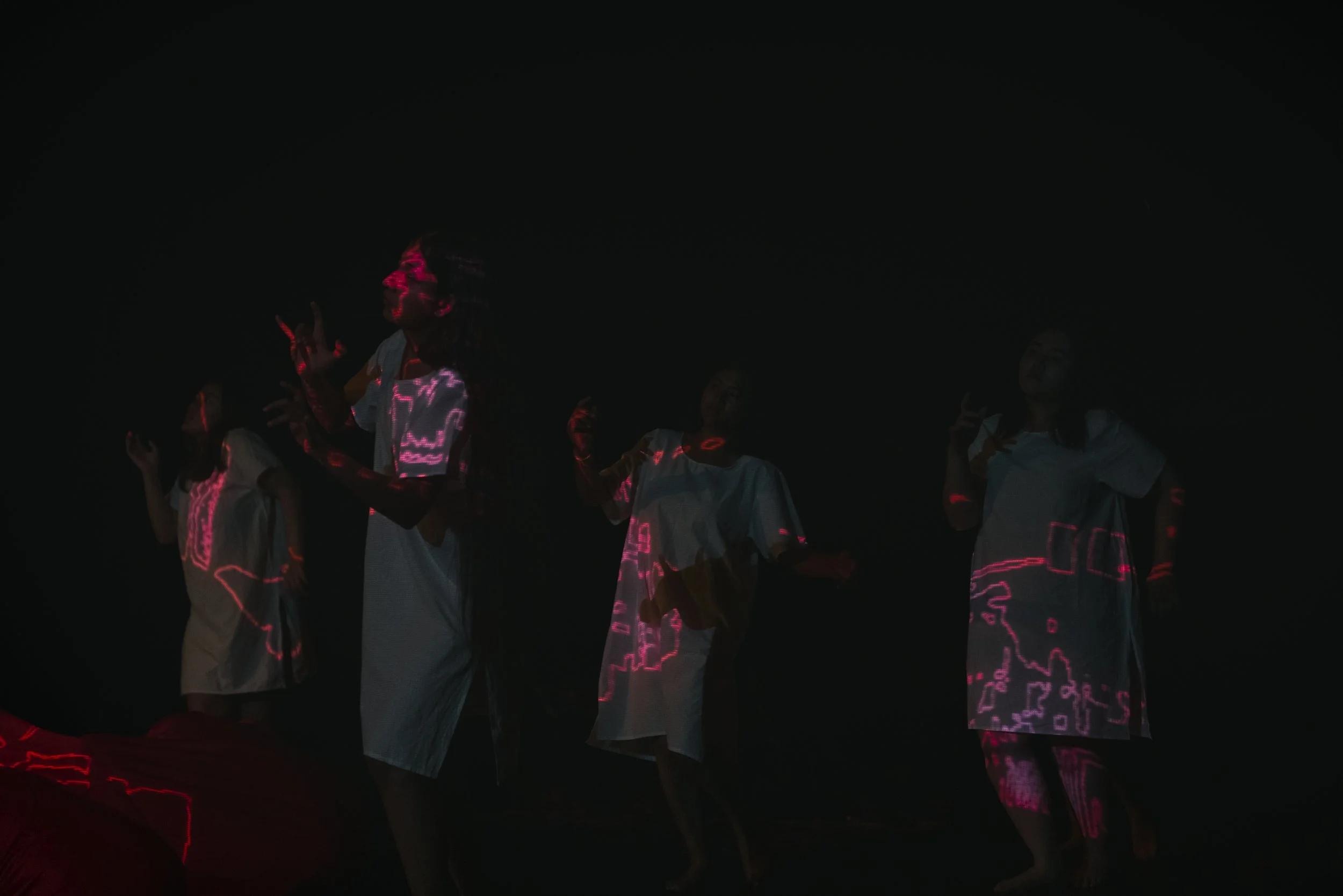 Group of people standing together in darkness with pink LED light projections on their faces and clothing.