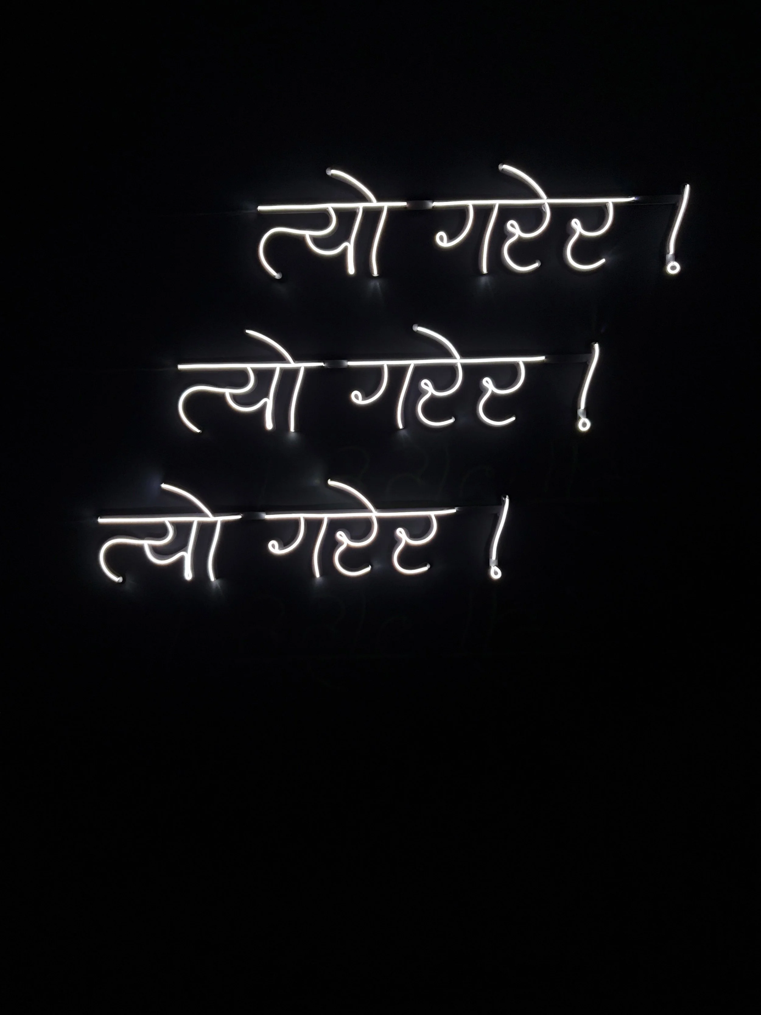 A neon sign with Devanagari text, lit in white against a dark background.