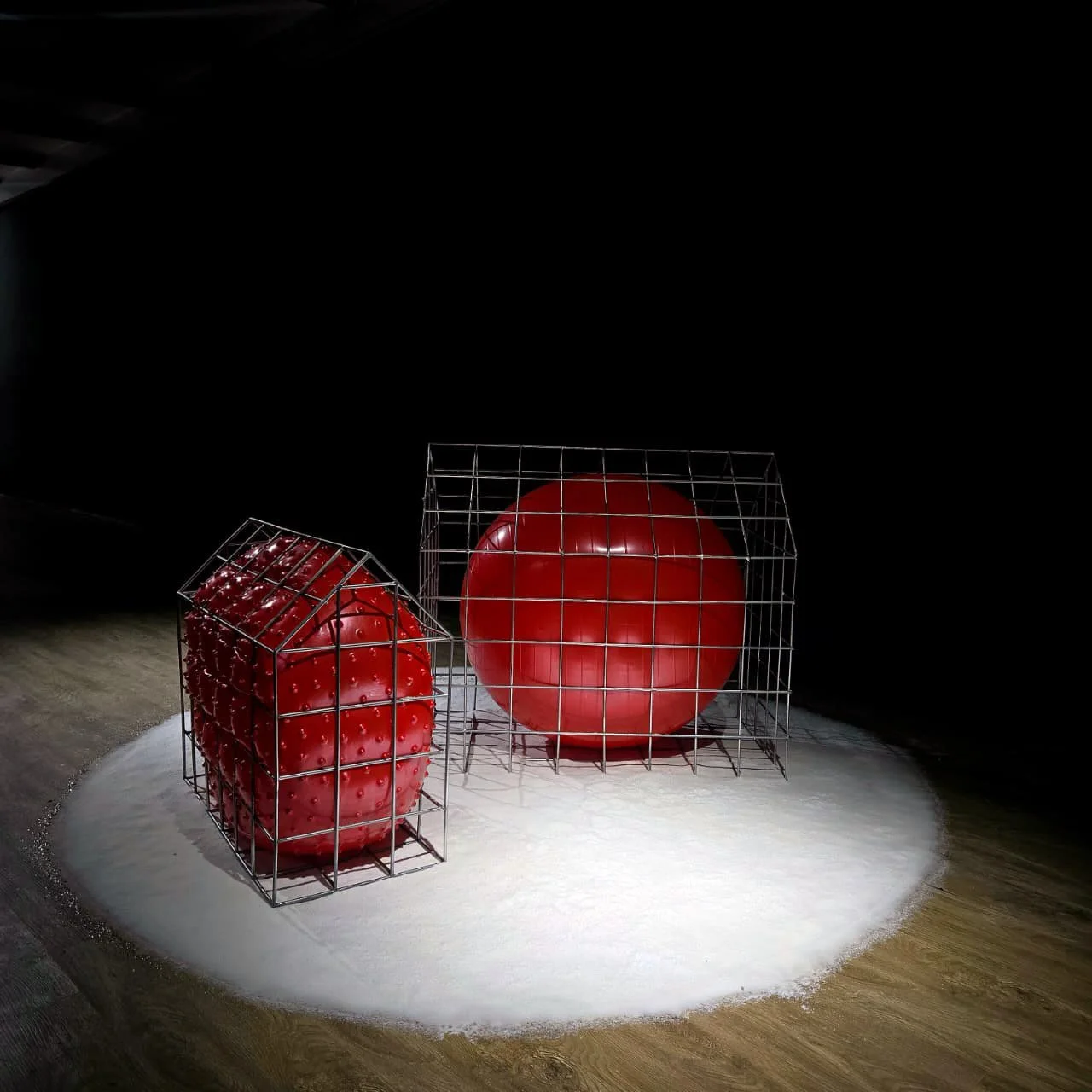 Two red strawberries inside metal cages with a red sphere, all set on a white surface against a dark background.