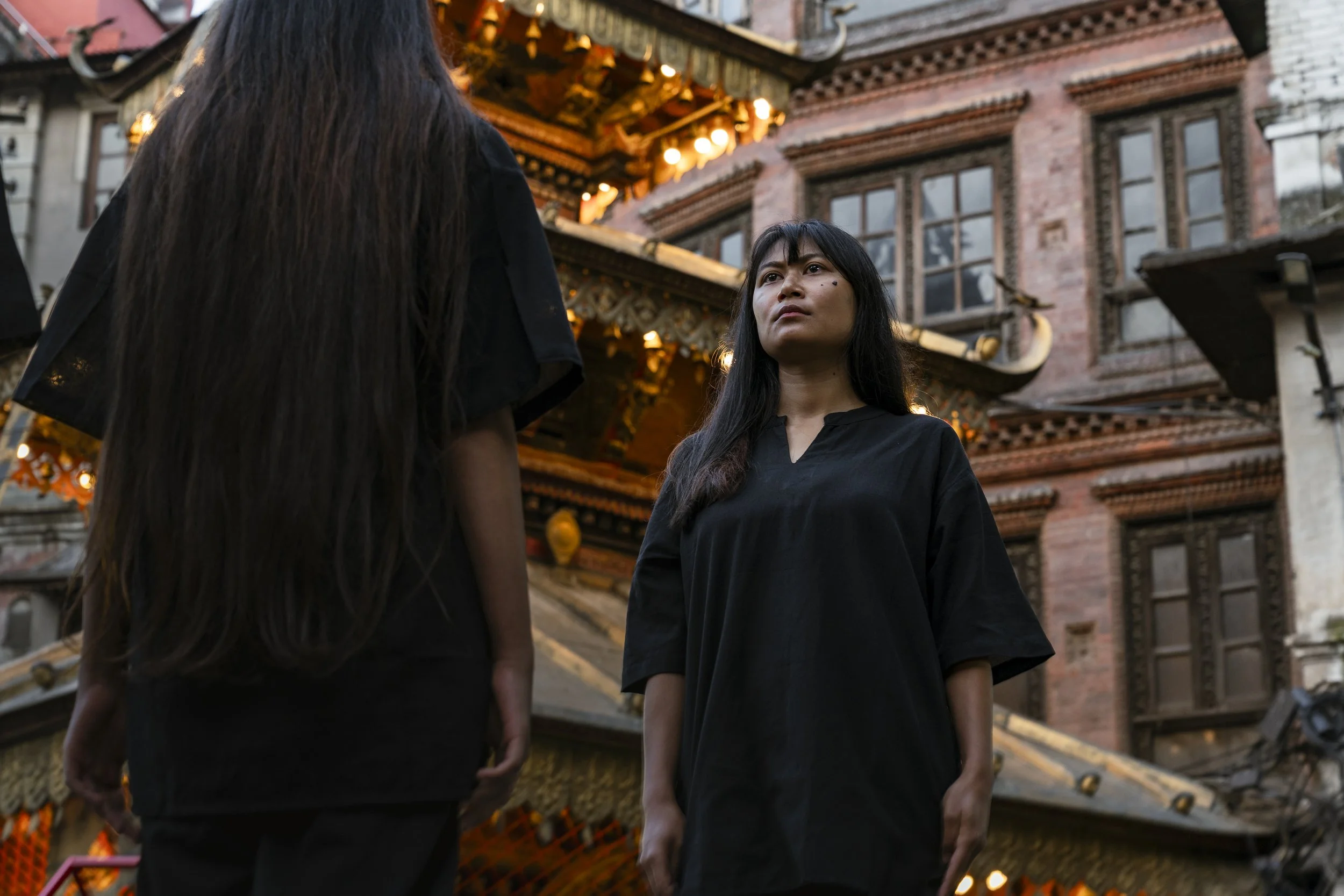 Two women, wearing black clothing, stand outside a decorated building with ornate architecture and glowing lights.