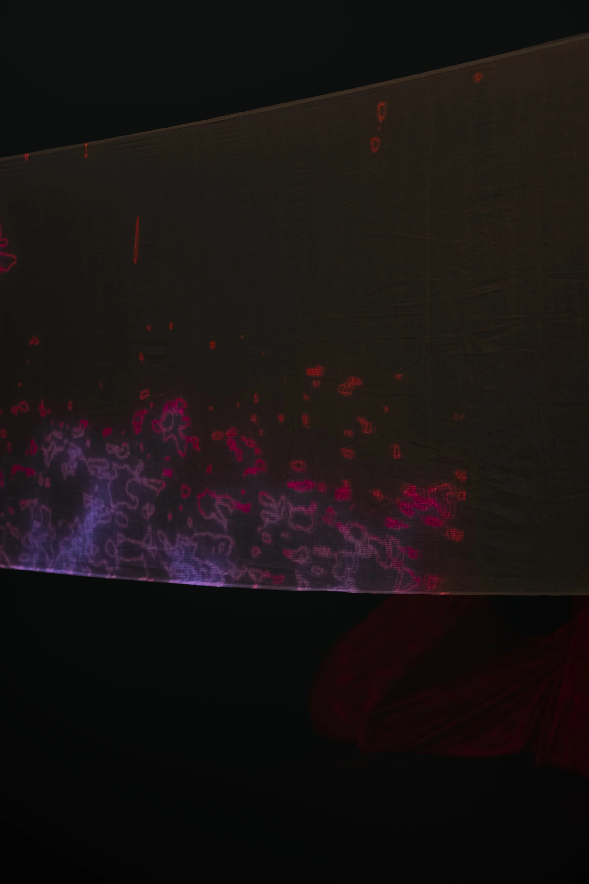 Close-up of a reflective surface displaying red and purple light patterns against a dark background, with part of a person's finger visible at the bottom right corner.