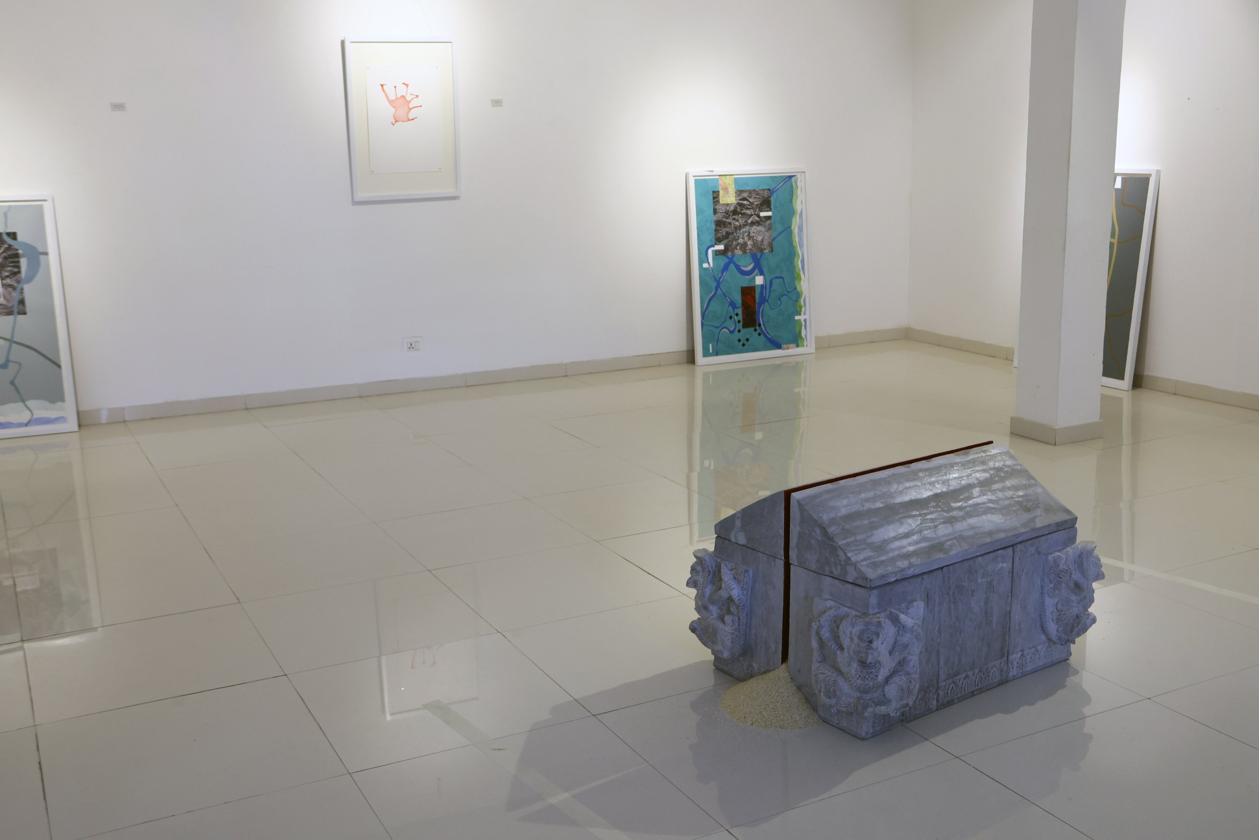 Art gallery with paintings on white walls and a gray marble sculpture on a carved pedestal in the foreground.