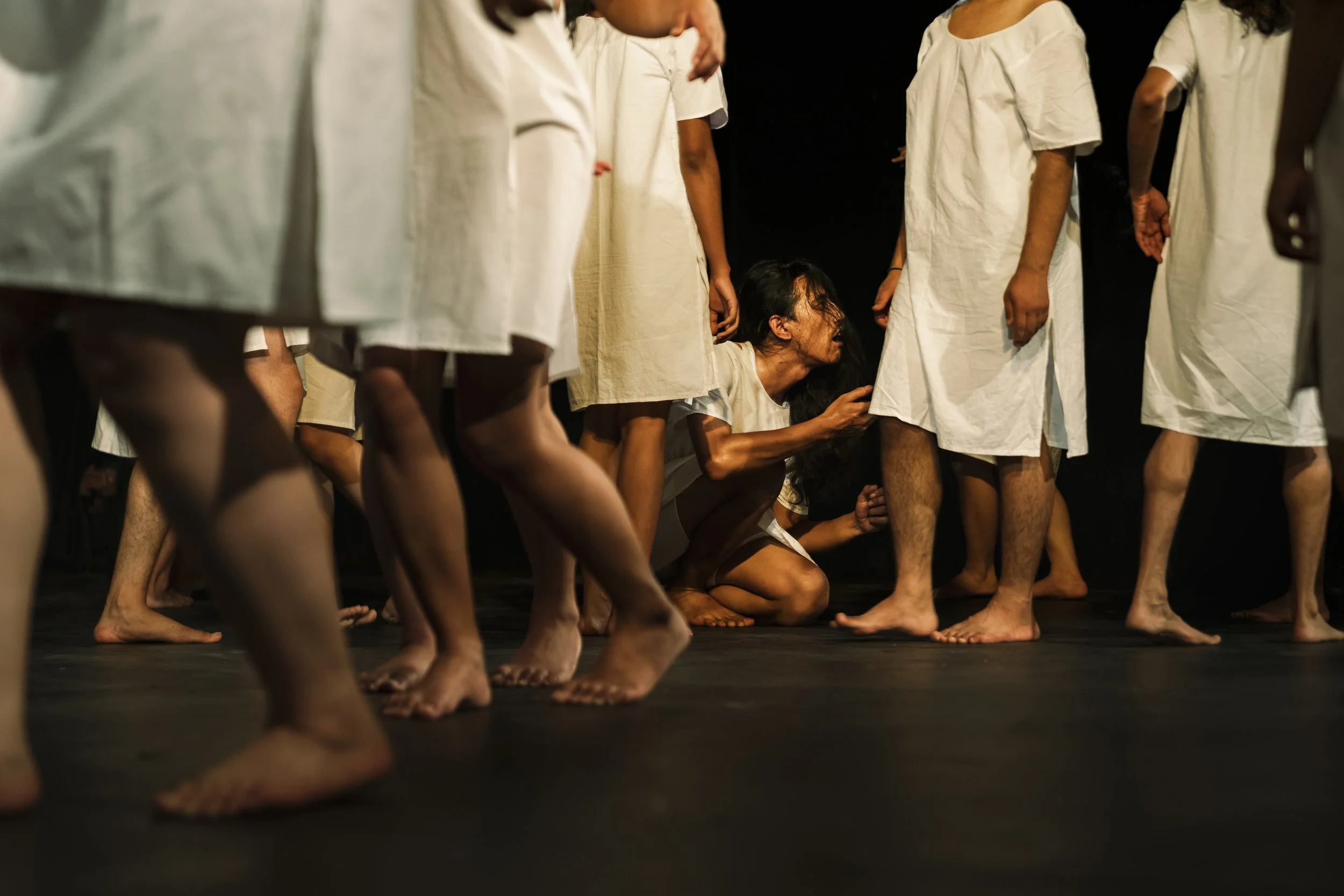A group of people dressed in white robes standing on a stage, with one person kneeling and appearing emotional among the others.