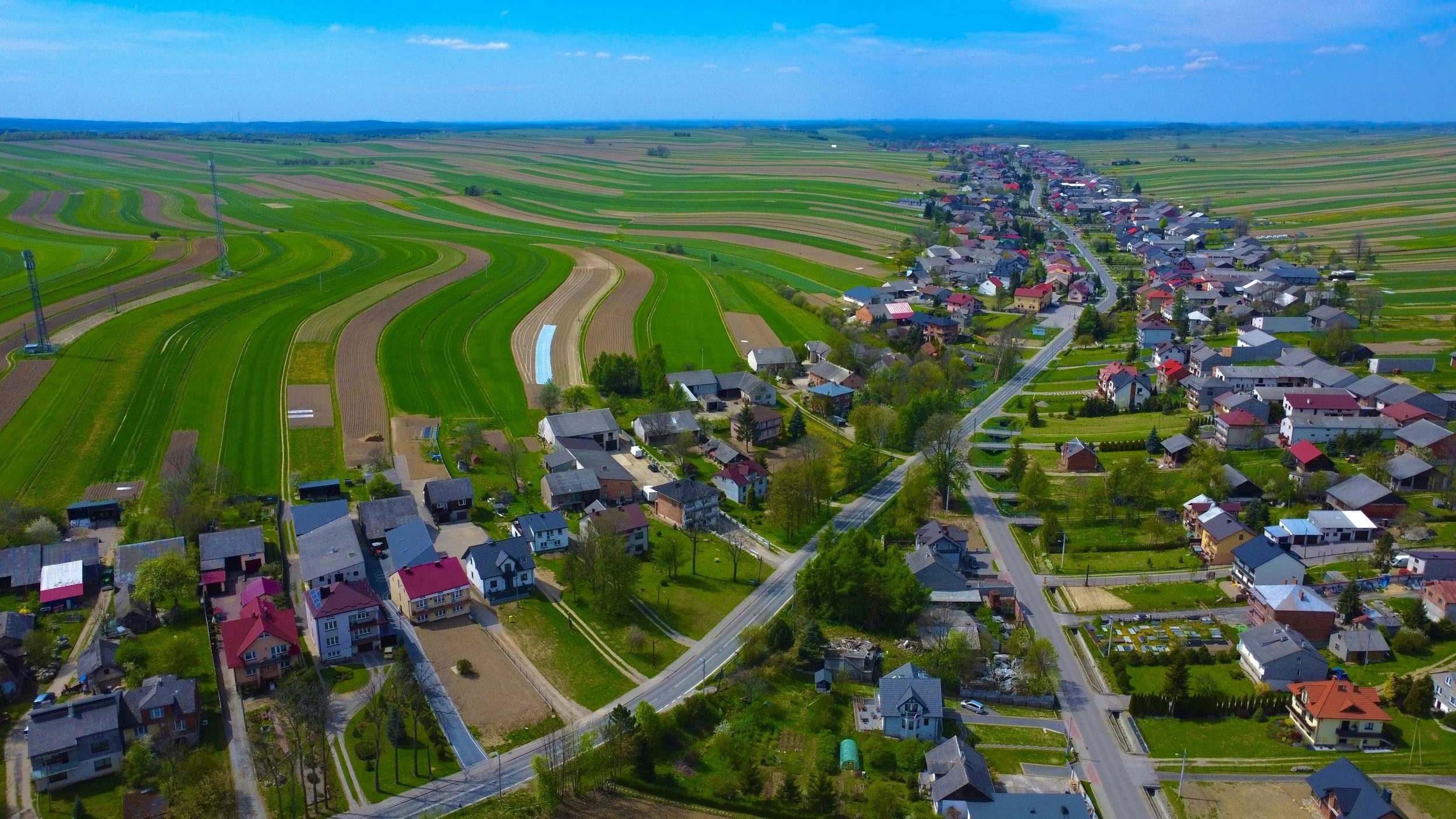 Aerial view of a small town with colorful houses surrounded by green fields and farmland under a blue sky.