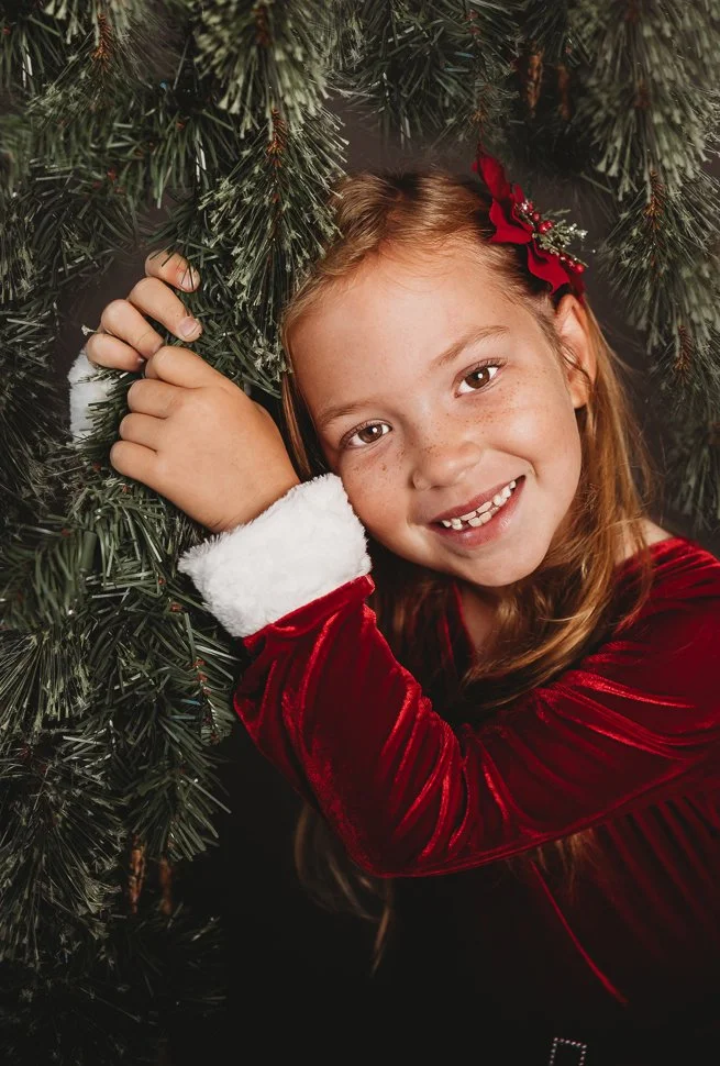 Blonde girl wearing Christmas velvet dress holding onto Winter Greenery